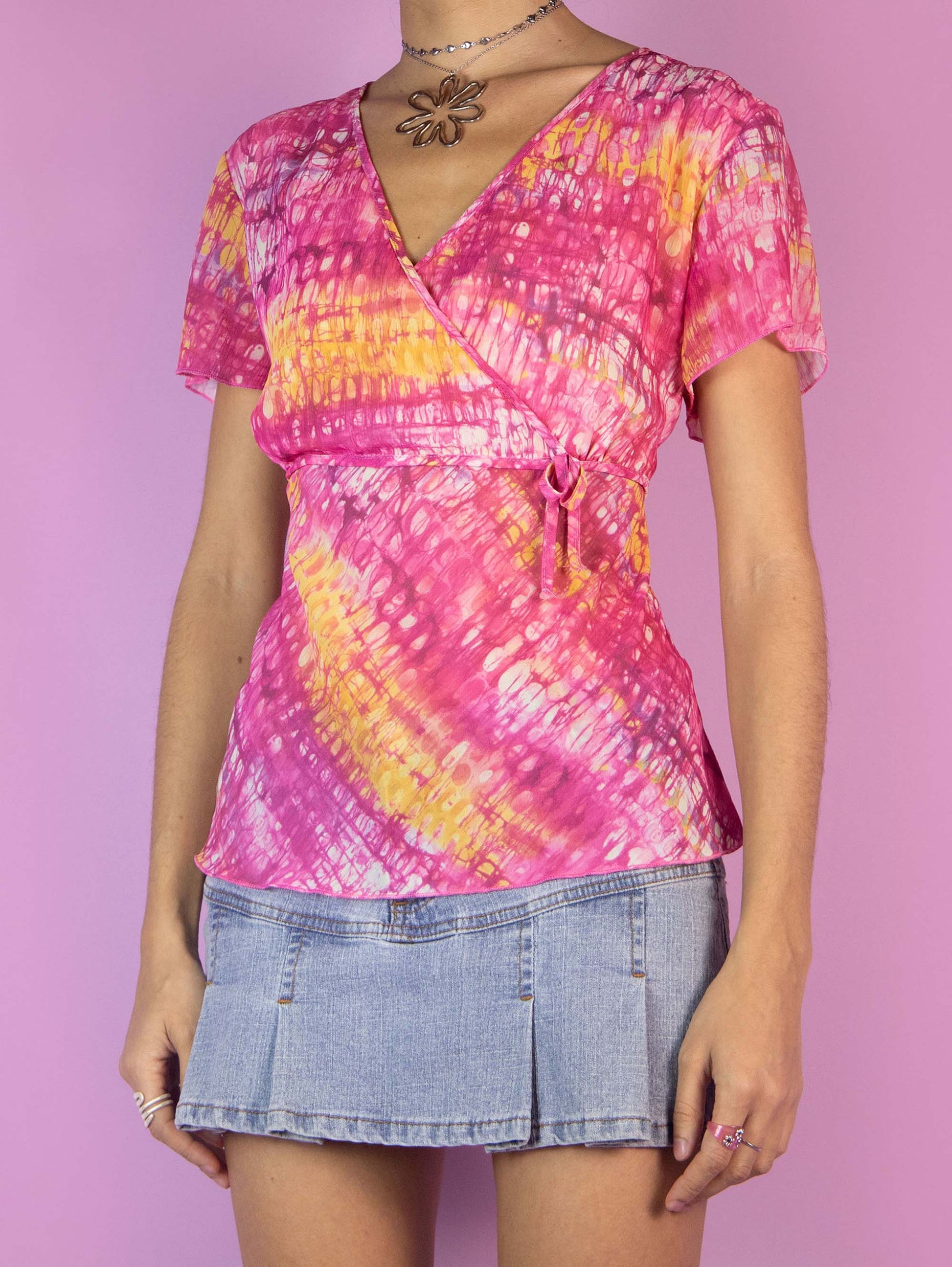 The Y2K Pink Sheer Graphic Top is a vintage short-sleeved shirt with an abstract pink and yellow tie-dye print, featuring a V-neckline. Cyber 2000s summer festival psychedelic blouse.