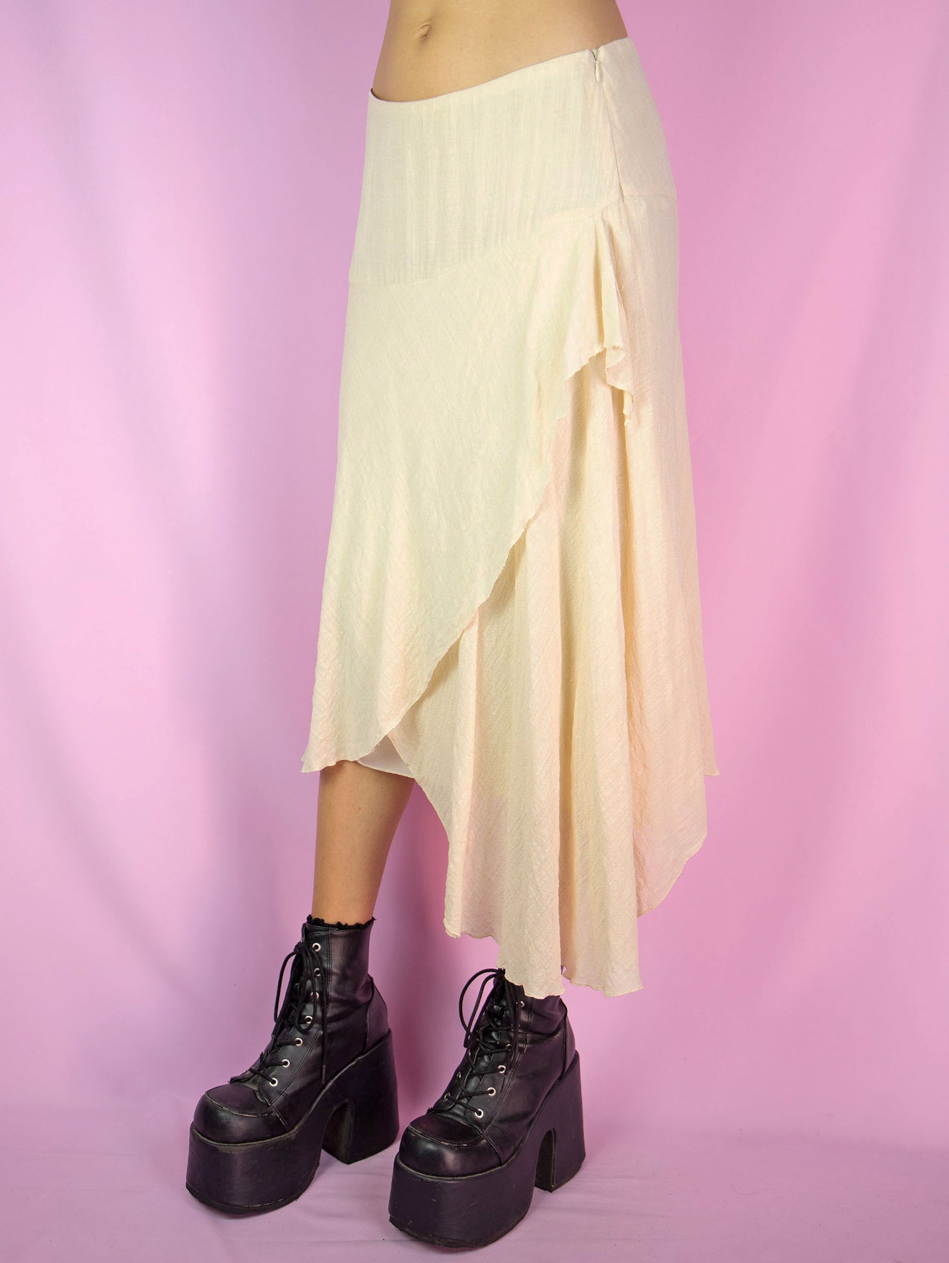 The Vintage 90s Beige Asymmetric Layered Skirt is a cream beige tiered layered skirt with an asymmetrical hem and a side zipper closure. Boho fairy grunge 1990s avant garde midi skirt.