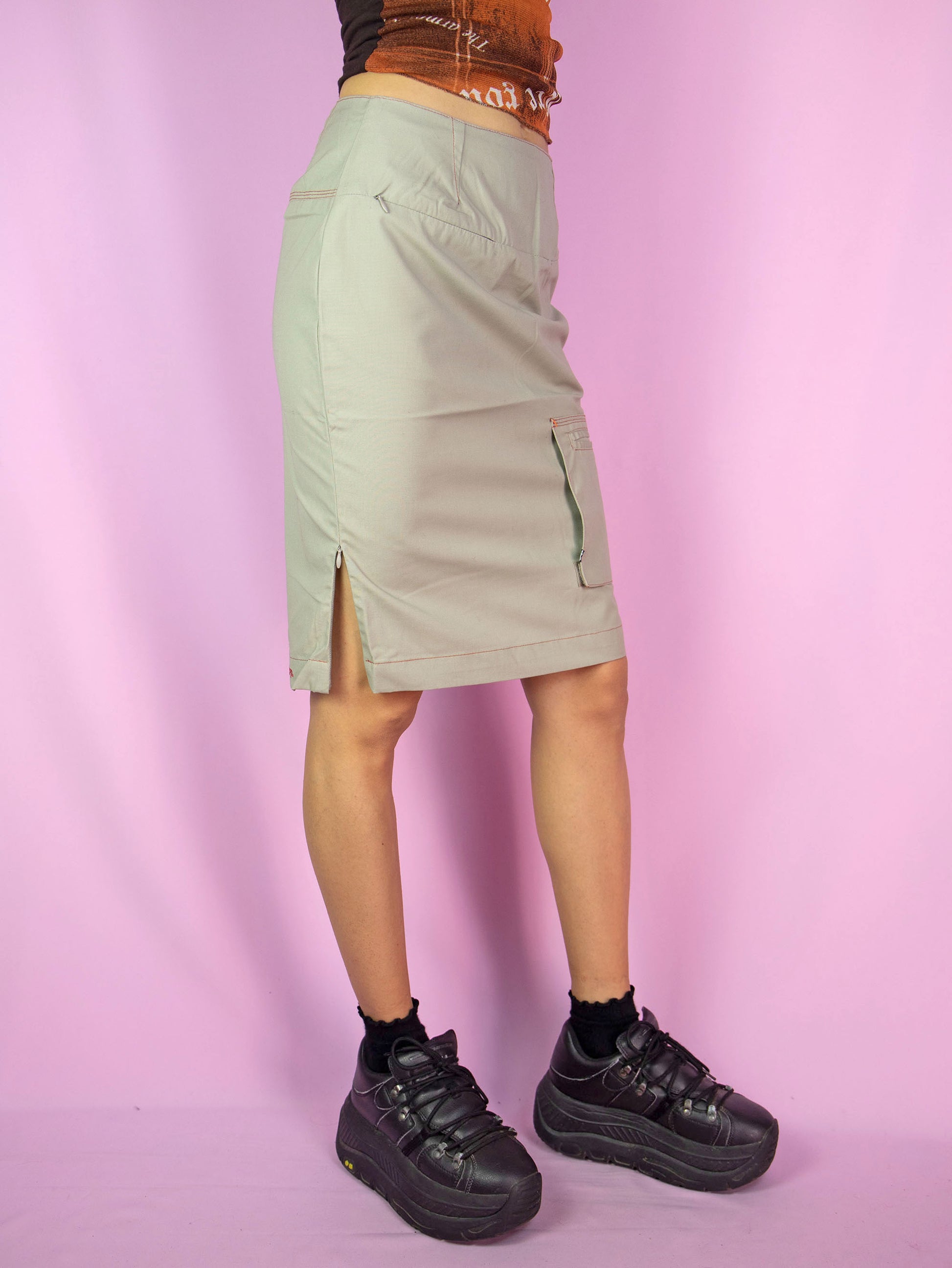 The Y2K Beige Grunge Cargo Skirt is a vintage skirt with pockets, a side zipper closure, and side slits with zippers. Cyber gorpcore 2000s utility mini skirt.