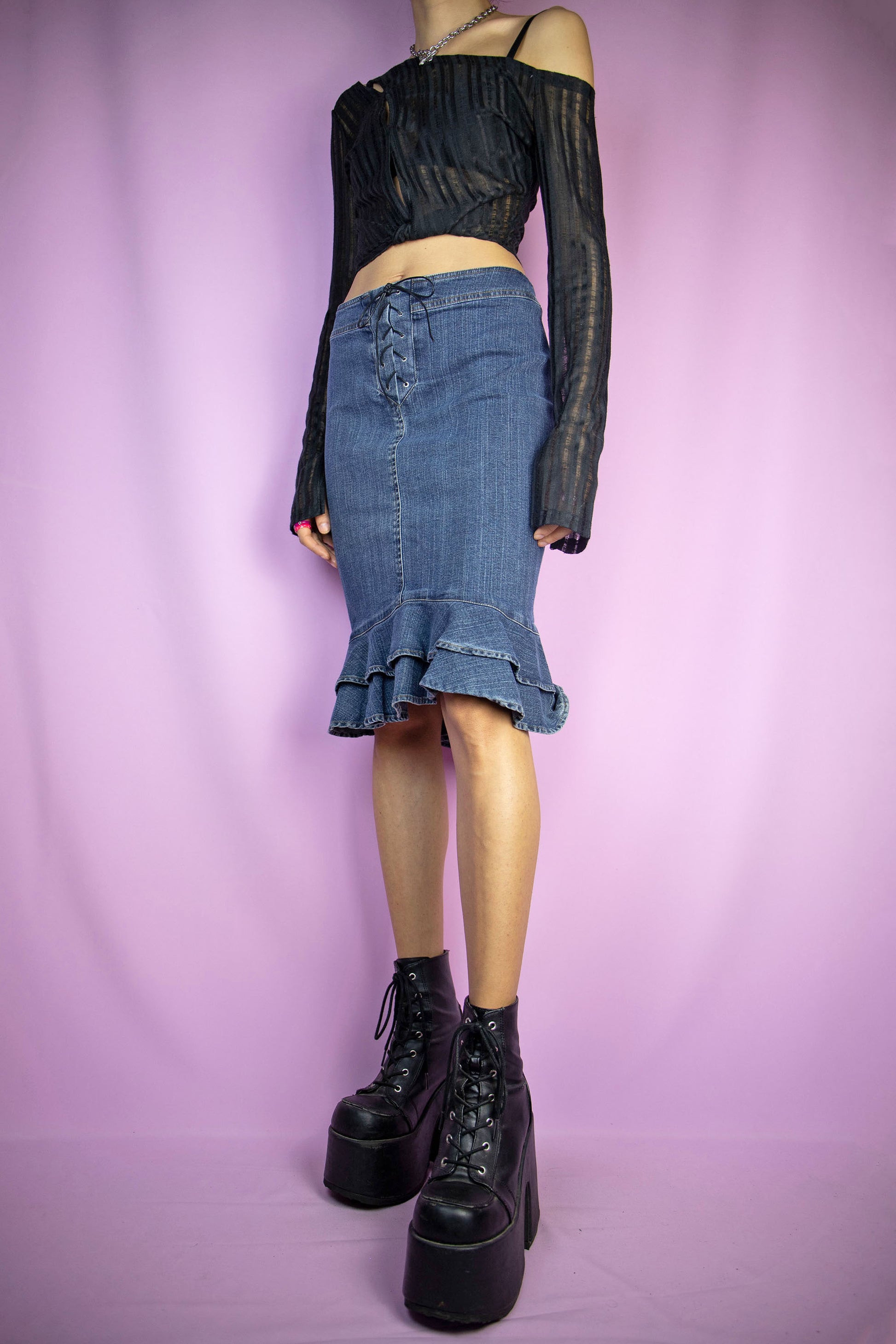 The Vintage Y2K Ruffle Hem Denim Skirt is a sleek dark denim trumpet skirt with a charming ruffled hem, back zipper closure, and lace-up tie front. This iconic cyber pencil jean mini skirt captures the essence of 2000s fashion.