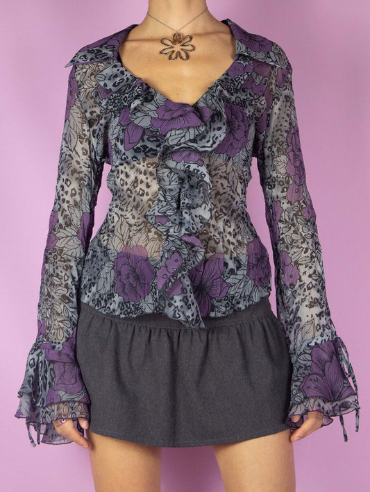 The Y2K Sheer Ruffle Blouse is a vintage romantic 2000s top featuring a semi-transparent gray, black, and purple floral and leopard animal print pattern. It has a V-neckline and bell sleeves.