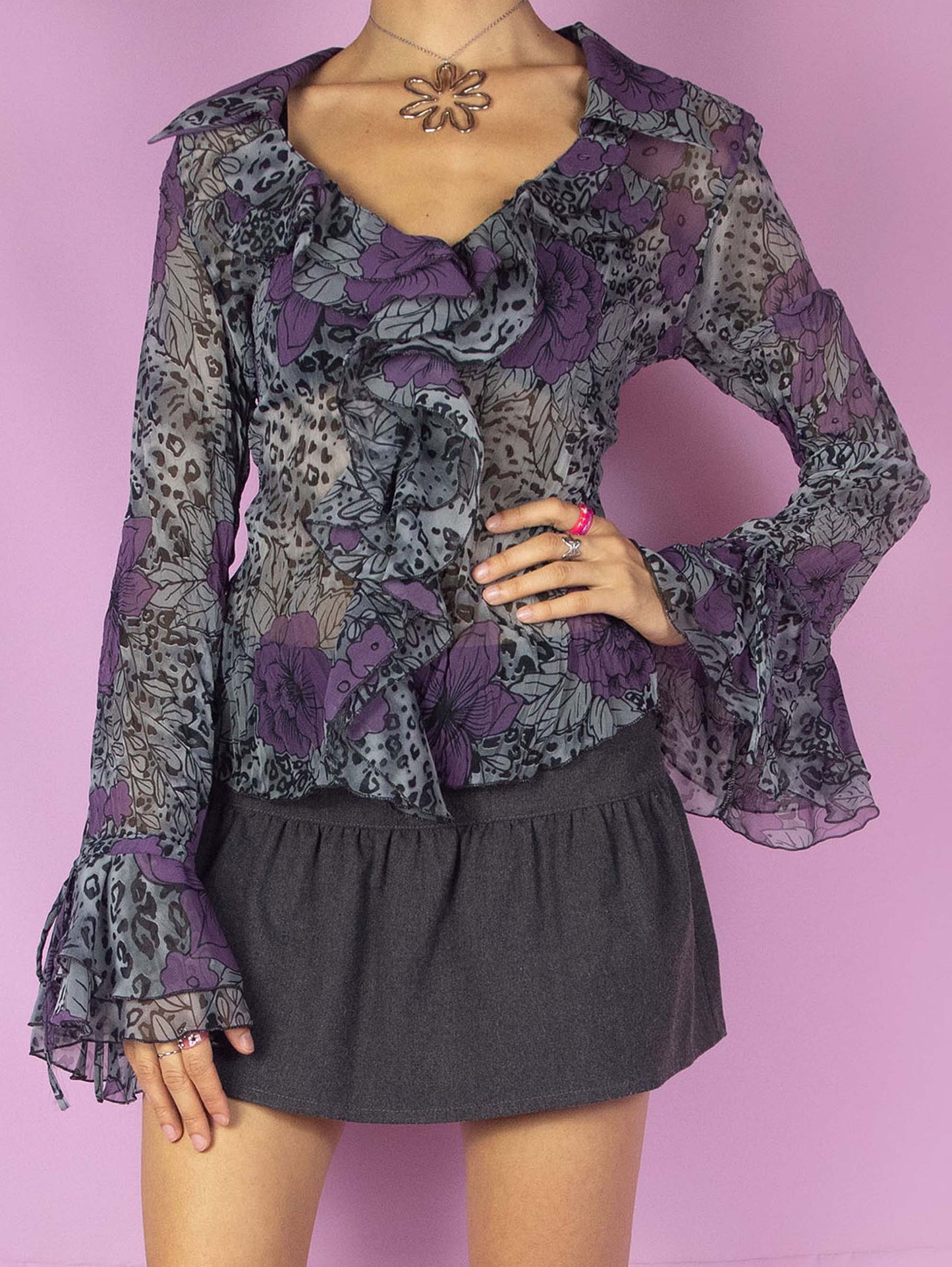 The Y2K Sheer Ruffle Blouse is a vintage romantic 2000s top featuring a semi-transparent gray, black, and purple floral and leopard animal print pattern. It has a V-neckline and bell sleeves.