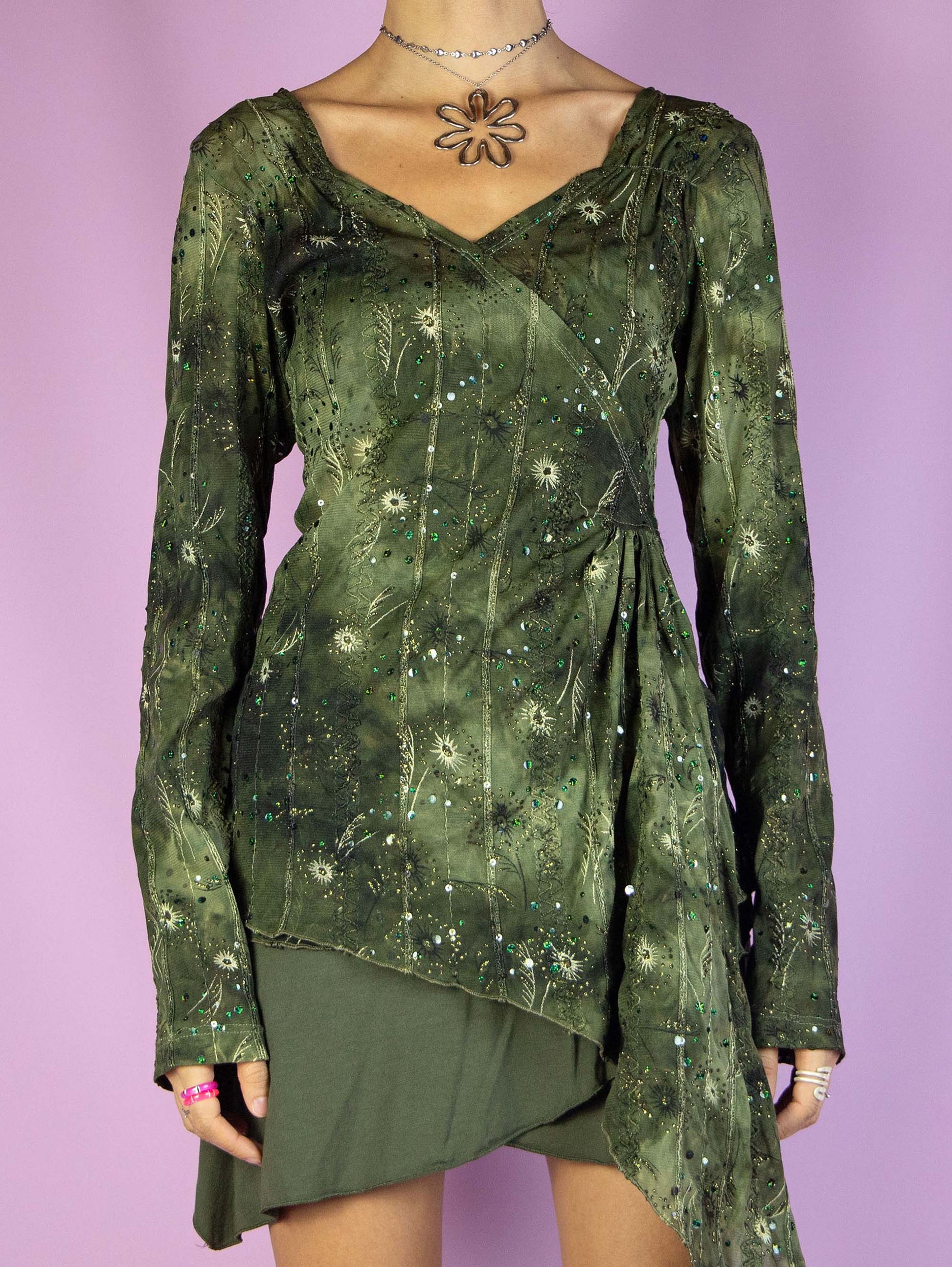 The Y2K Fairy Grunge Mesh Top is a vintage long-sleeved asymmetrical draped mesh shirt in green tie-dye effect with embroidered, glitter, and sequin details. Stunning cyber festival rave 2000s shirt.
