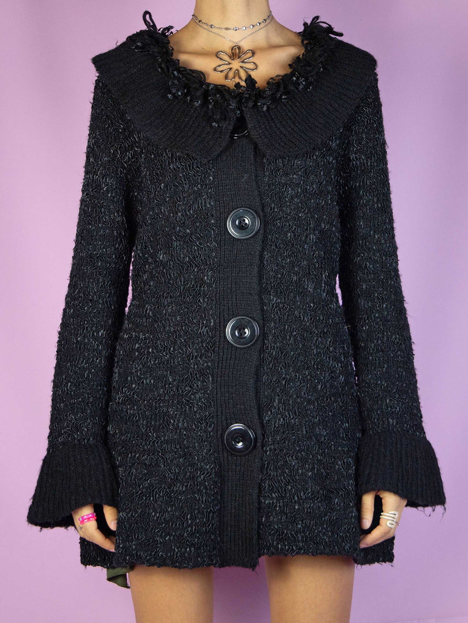 The Y2K Black Knit Cardigan is a vintage 2000s fairy goth inspired winter chunky knit sweater with a flared hem, collar, big buttons, and bell sleeves.