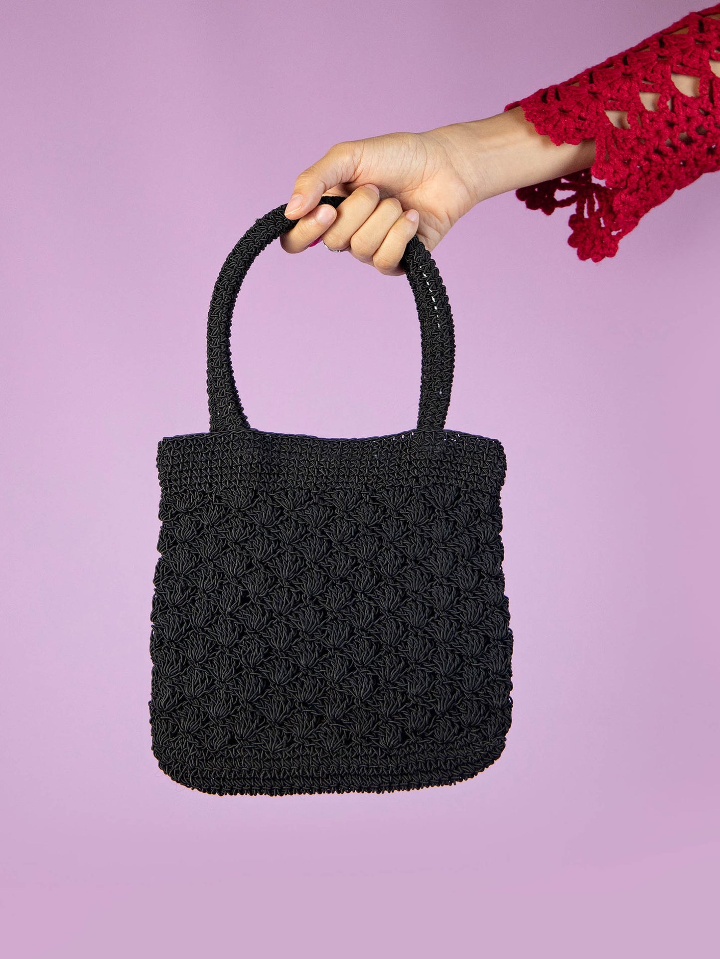 The Y2K Black Crochet Mini Bag is a vintage black handbag with a top handle, crafted in a crochet-style with a zipper closure. Super cute boho 2000s party mini bag.