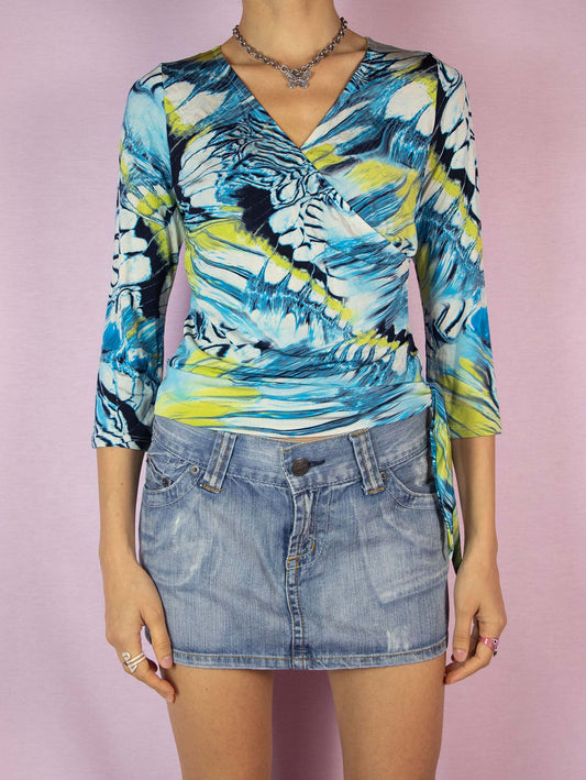 The Y2K Abstract Print Wrap Top is a vintage 2000s festival-style shirt with a multicolored blue abstract graphic pattern, half sleeves, and a V-neckline. Made in Spain.