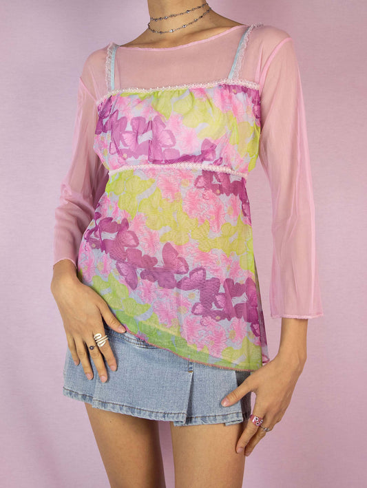 The Y2K Pink Printed Mesh Top is a vintage 2000s romantic fairy cottagecore light pink and green semi-sheer top with floral and butterfly graphics, three-quarter sleeves, and an asymmetric hem. Excellent vintage condition.