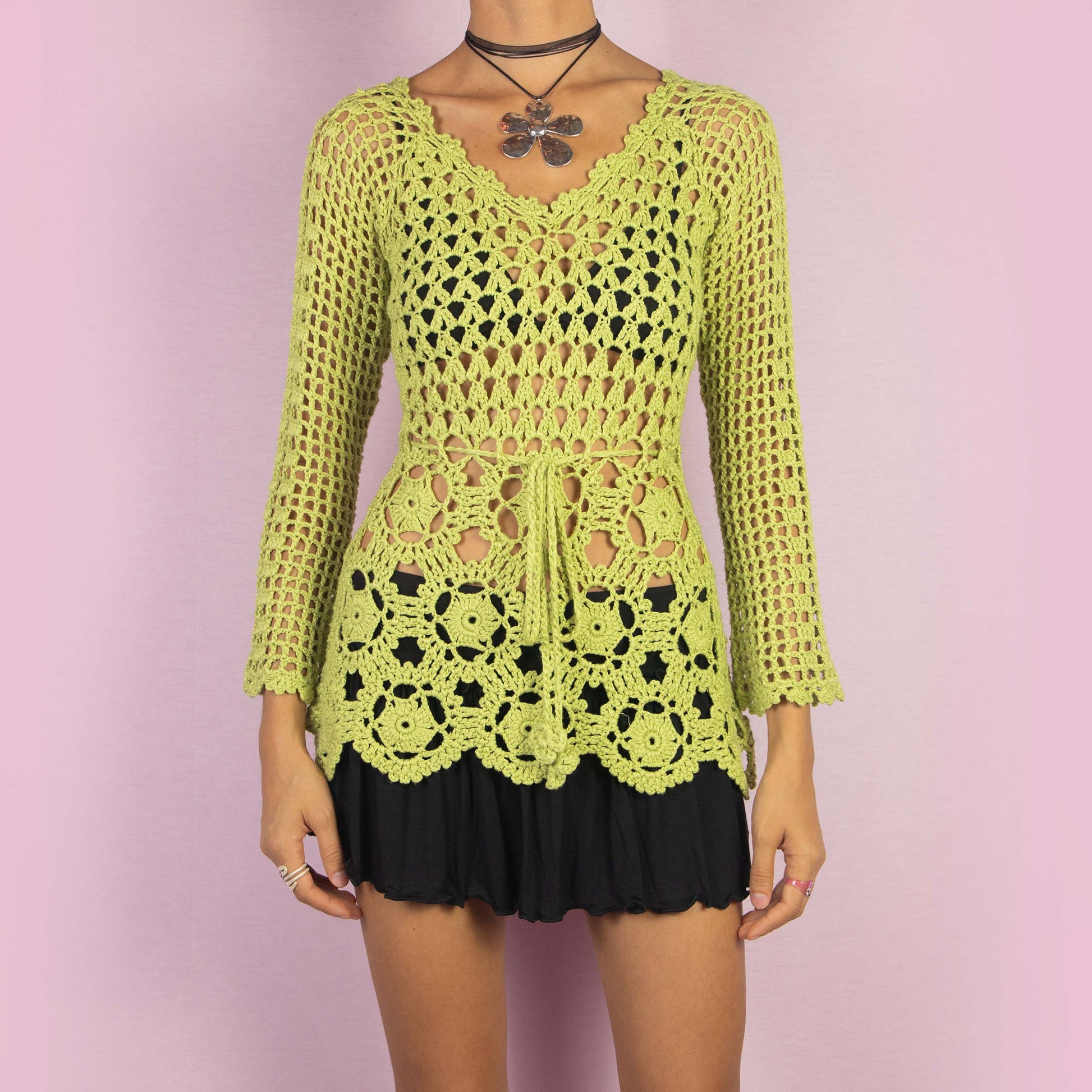 The Y2K Green Crochet Sweater is a vintage 2000s top featuring an open-knit, intricate crochet pattern and a tie-front detail at the waist. A perfect layering piece for a spring or summer casual or beach look.