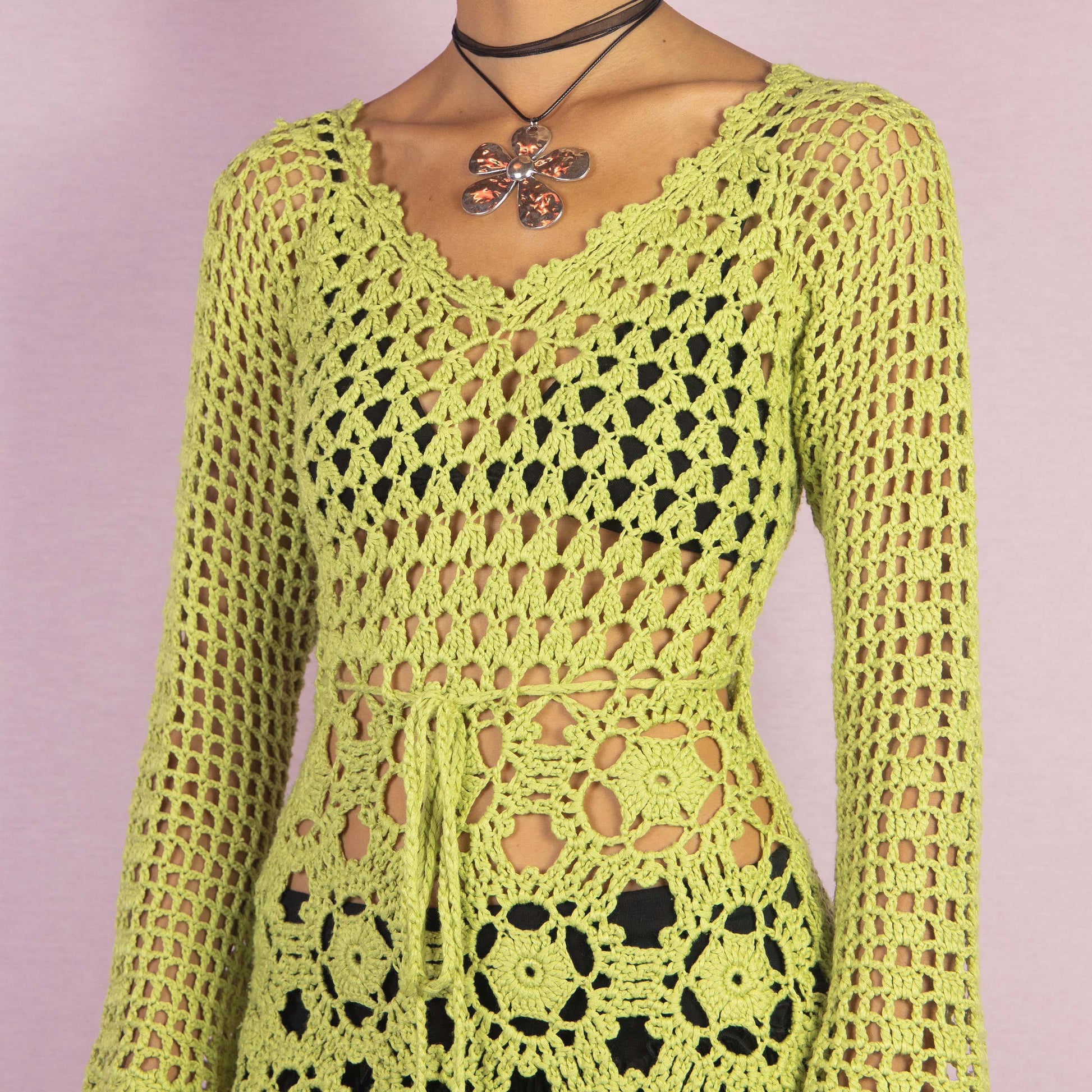 The Y2K Green Crochet Sweater is a vintage 2000s top featuring an open-knit, intricate crochet pattern and a tie-front detail at the waist. A perfect layering piece for a spring or summer casual or beach look.