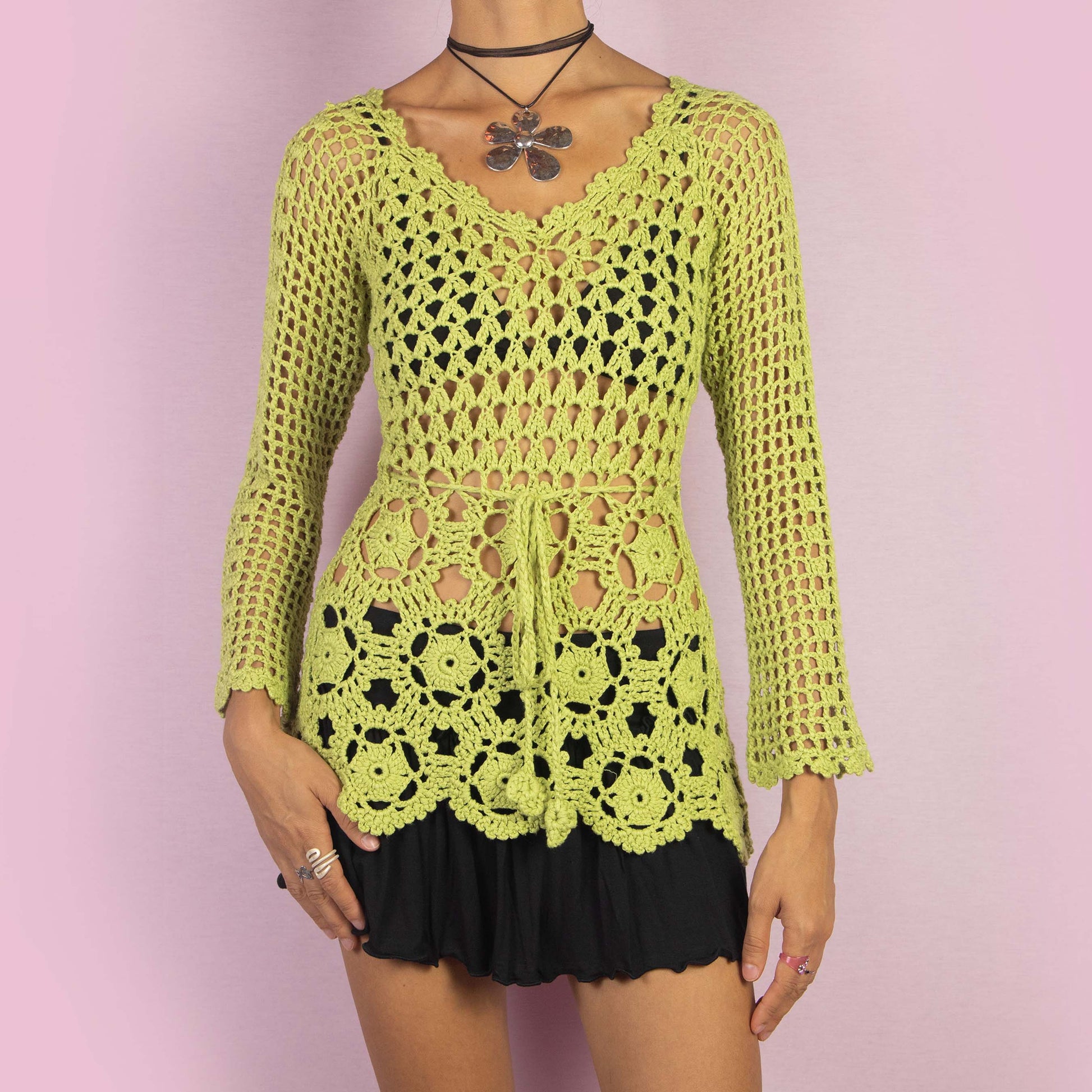 The Y2K Green Crochet Sweater is a vintage 2000s top featuring an open-knit, intricate crochet pattern and a tie-front detail at the waist. A perfect layering piece for a spring or summer casual or beach look.