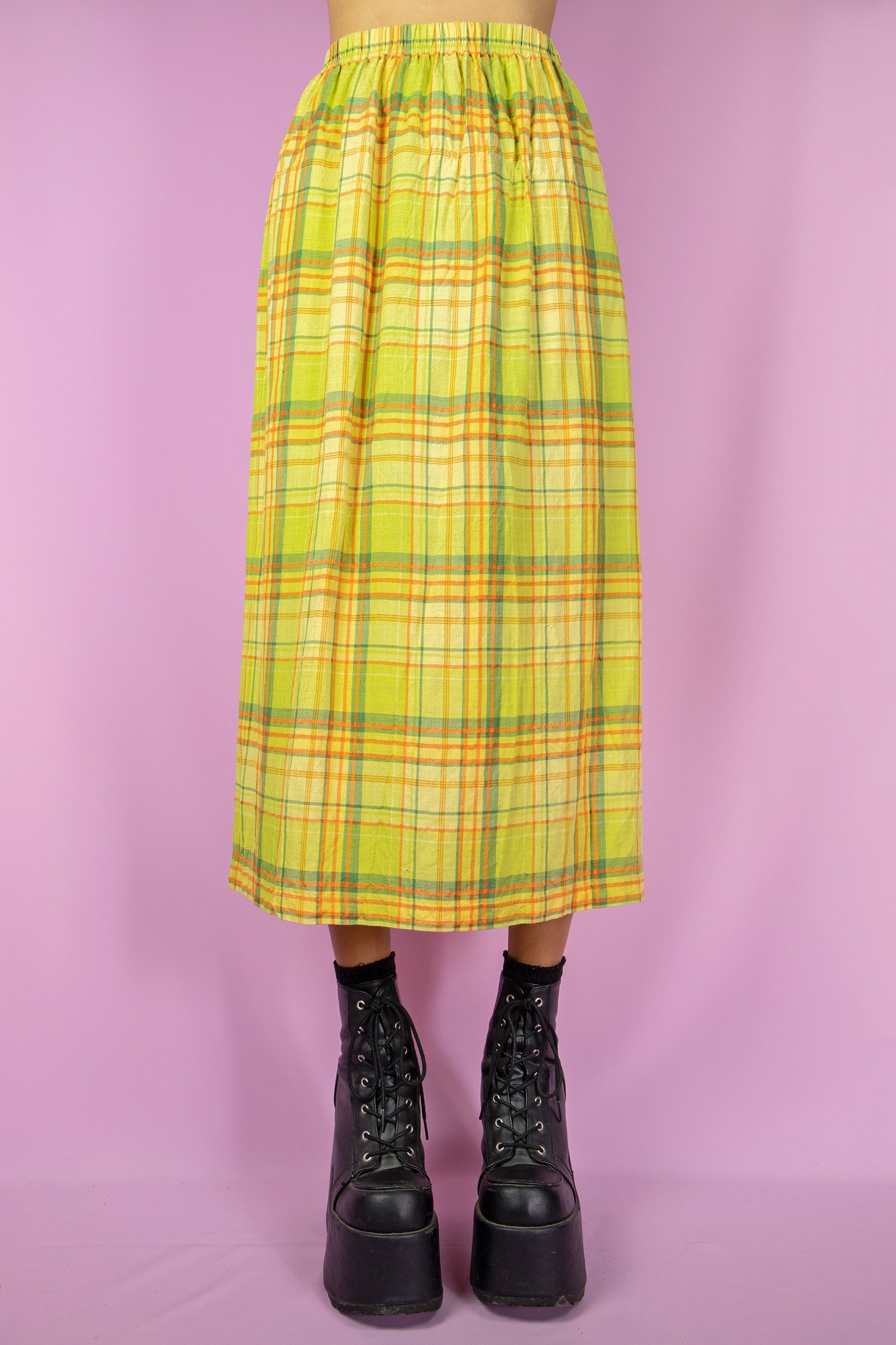 The Vintage 90s Green Plaid Midi Skirt is a long, green, yellow, and orange checkered skirt featuring a side slit and elastic waist. Cottage prairie 1990s boho summer skirt.