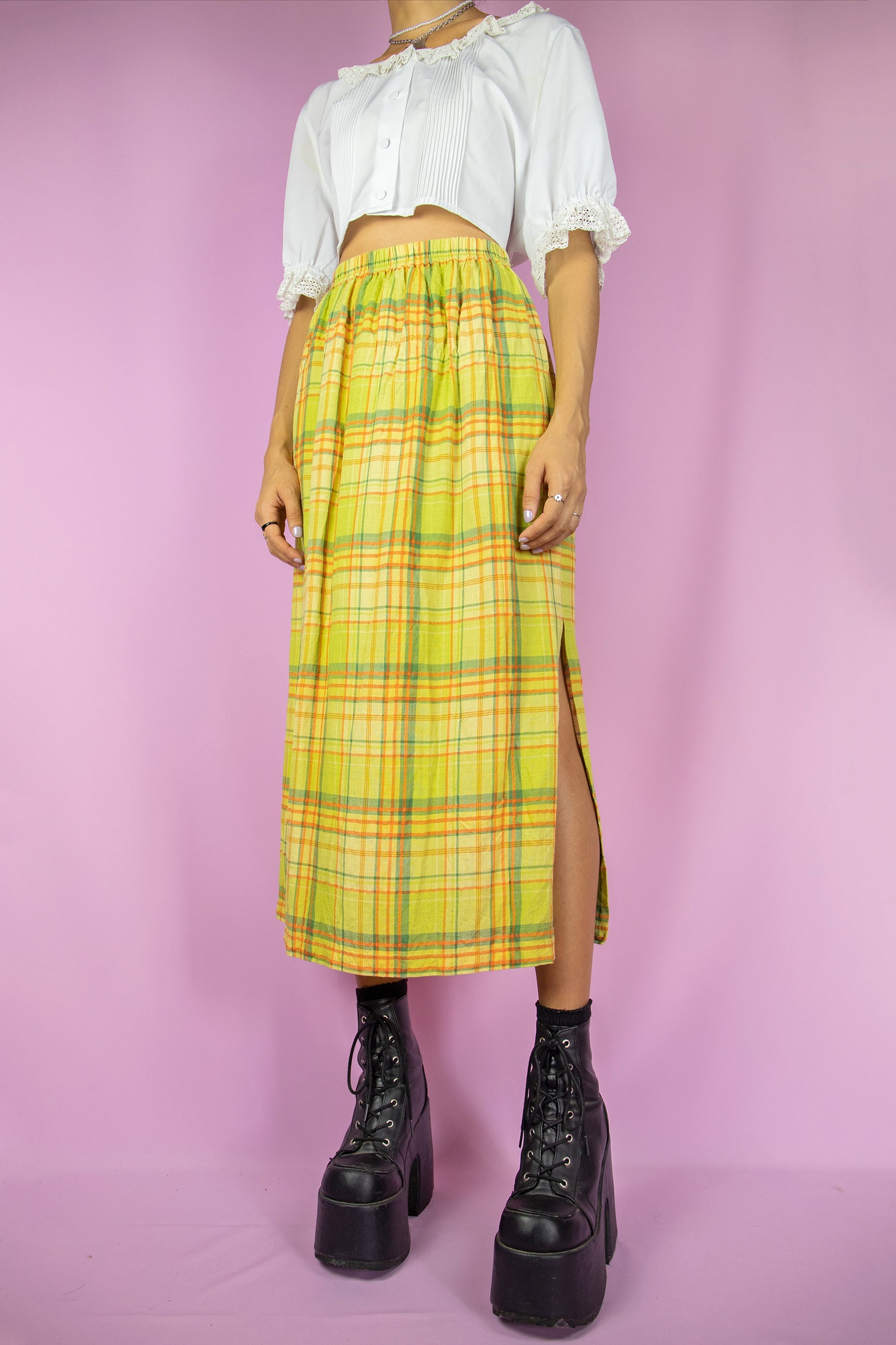 The Vintage 90s Green Plaid Midi Skirt is a long, green, yellow, and orange checkered skirt featuring a side slit and elastic waist. Cottage prairie 1990s boho summer skirt.