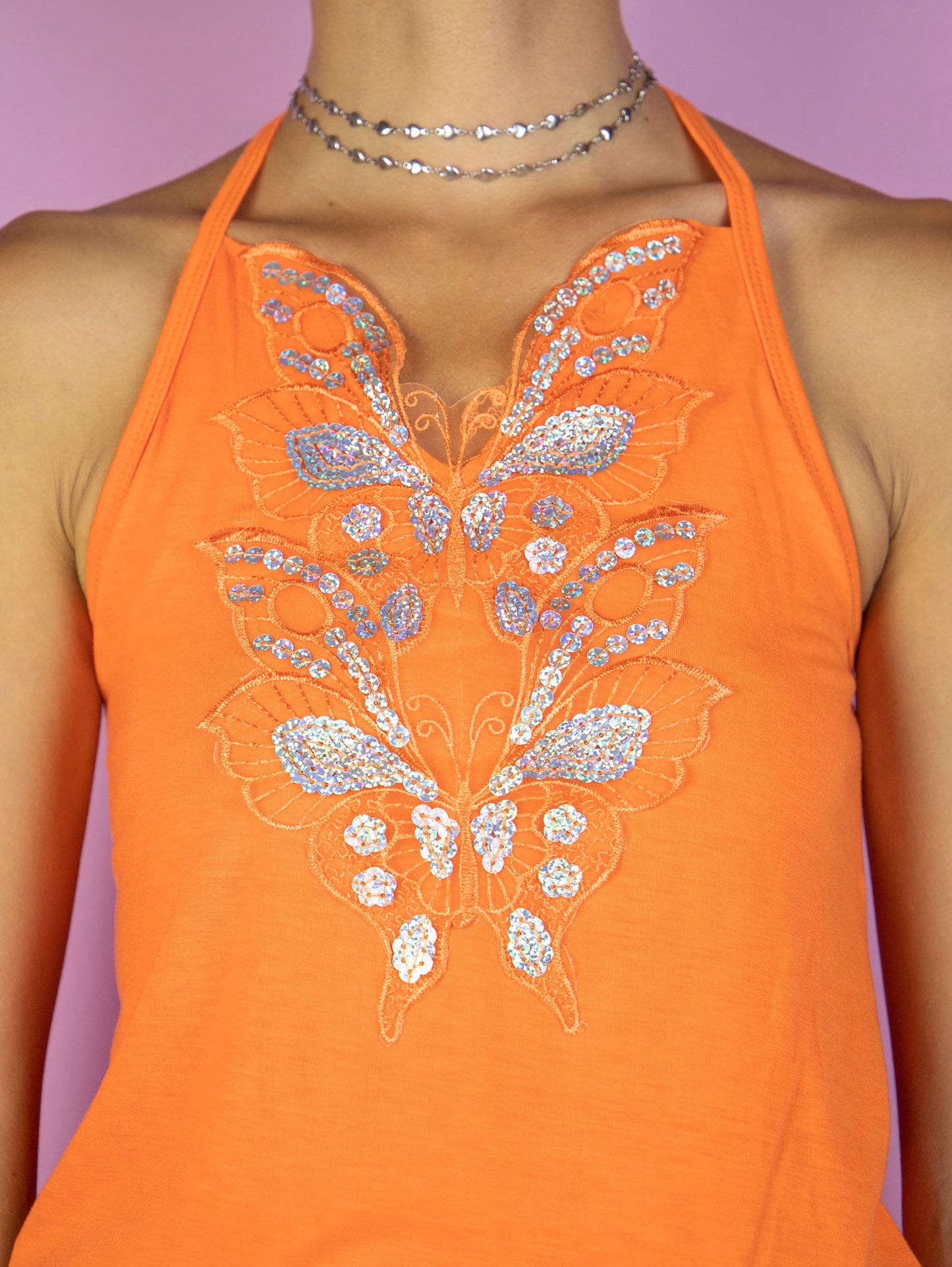 The Y2K Orange Halter Top is a vintage 2000s cyber summer festival butterfly detail halter tie neck top embellished with shiny sparkle silver sequins.