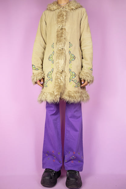 The Vintage Y2K Beige Afghan Inspired Coat is a light brown corduroy coat featuring a faux fur collar and cuffs, zip and button closure, pockets, and embroidered details. This iconic penny lane style winter coat from the 2000s serves as a boho fairy grunge statement jacket.