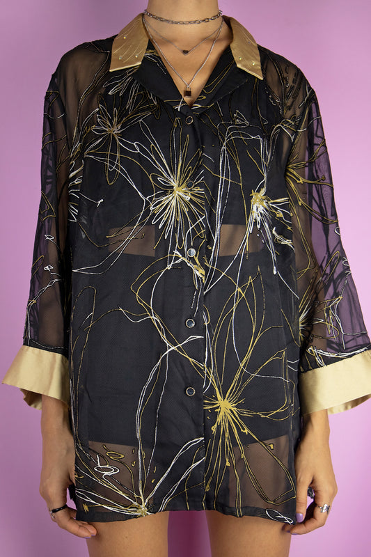 The Vintage 90's Black Gold Sheer Blouse is an elegant abstract semi-sheer black and gold top with a collar and buttons. Achieve a stylish oversized look, or wear it as a flowy duster jacket. This versatile piece is perfect for an elegant party night, capturing the essence of the 1990s.