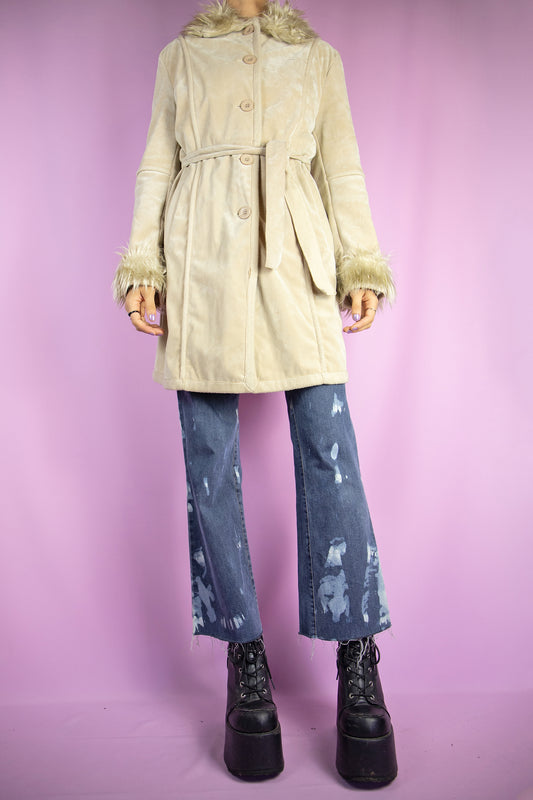 The Vintage Y2K Beige Faux Suede Fur Coat is a beige faux suede coat showcasing faux fur collar and cuffs, along with pockets, buttons, and a coordinating belt. This iconic penny lane afghan style winter coat from the 2000s stands as a gorgeous cyber statement jacket.