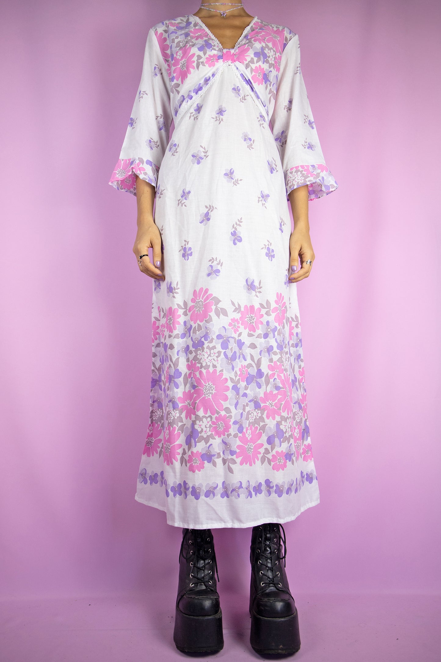 The Vintage 80s Boho White Midi Dress is a summer bell sleeve kaftan maxi dress with a pink and purple floral pattern and a v-neck.