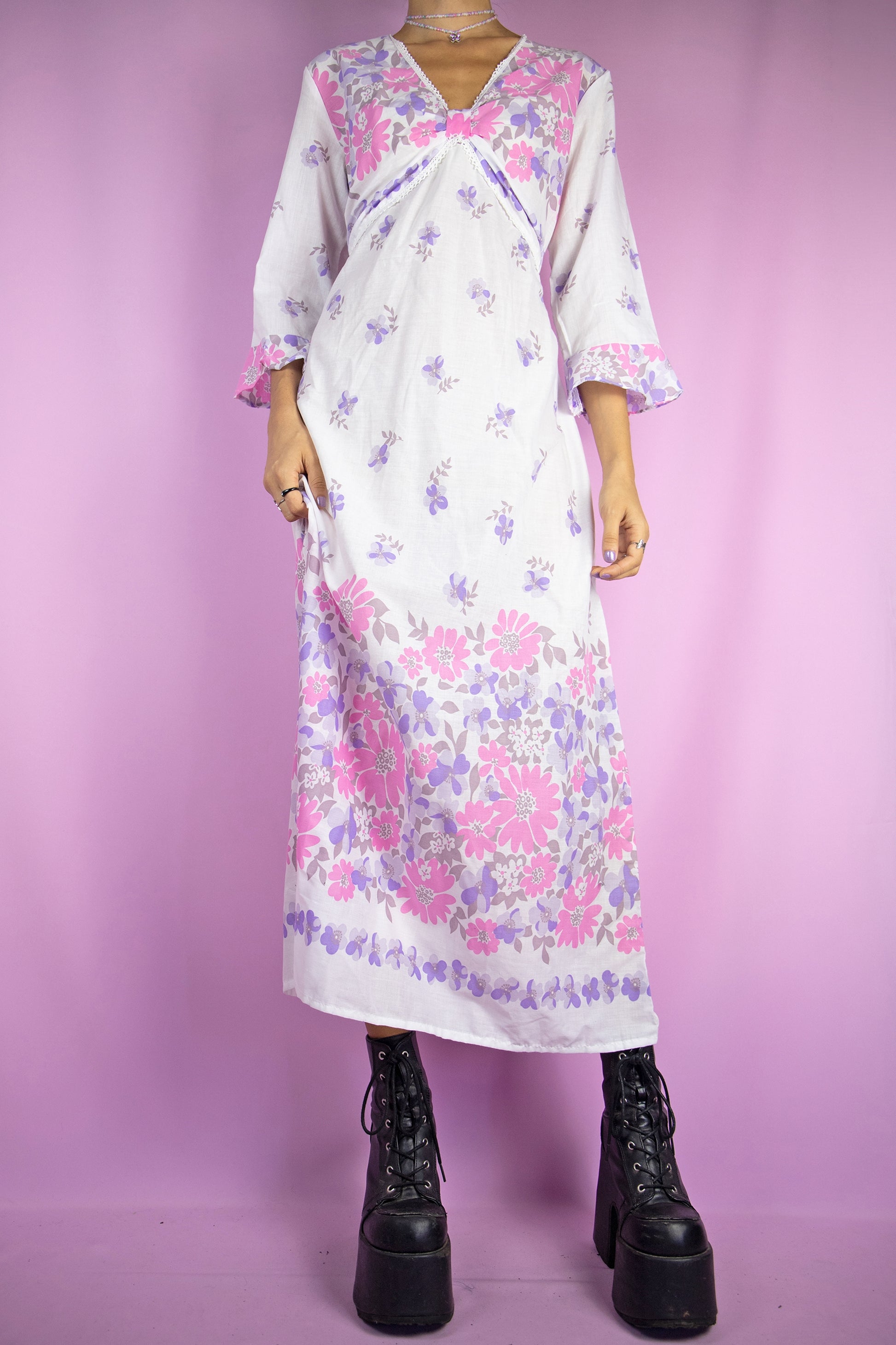 The Vintage 80s Boho White Midi Dress is a summer bell sleeve kaftan maxi dress with a pink and purple floral pattern and a v-neck.
