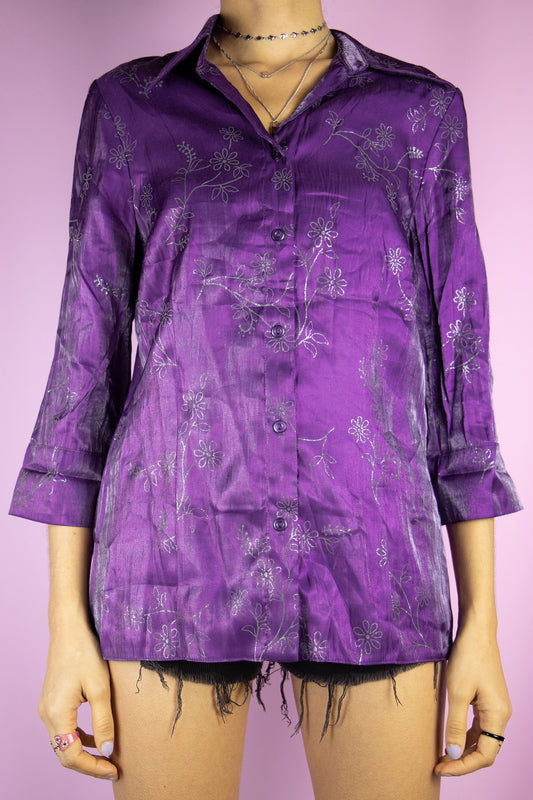 The Y2K Purple Iridescent Blouse is a vintage iridescent shimmering purple top with three-quarter sleeves, a collar, buttons, and silver glitter floral detailing. Elegant boho 2000s party night shirt.