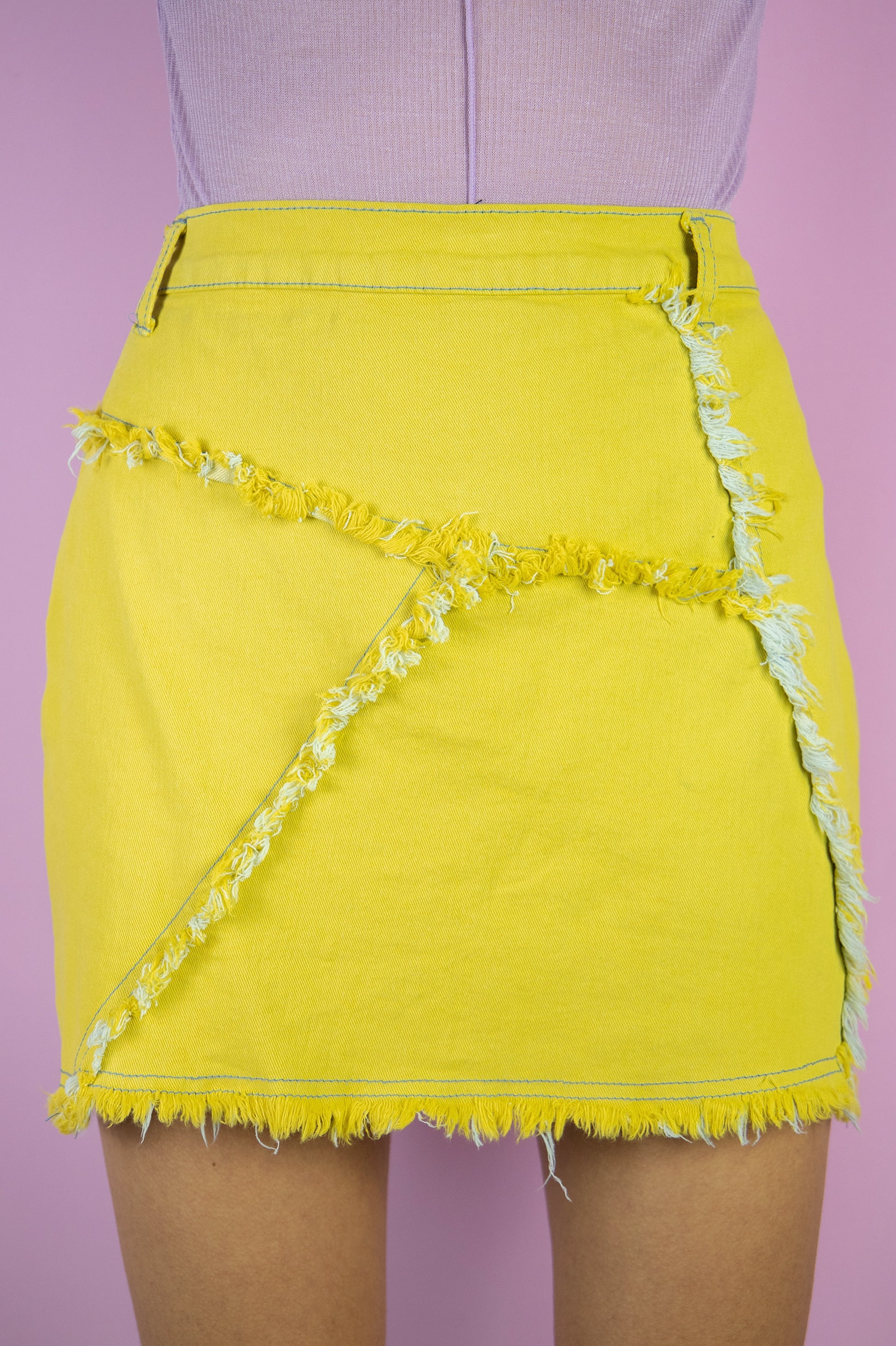 The Y2K Cyber Yellow Mini Skirt is a vintage stretchy yellow asymmetric skirt with frayed raw-edge detail. Subversive grunge 2000s mini skirt.