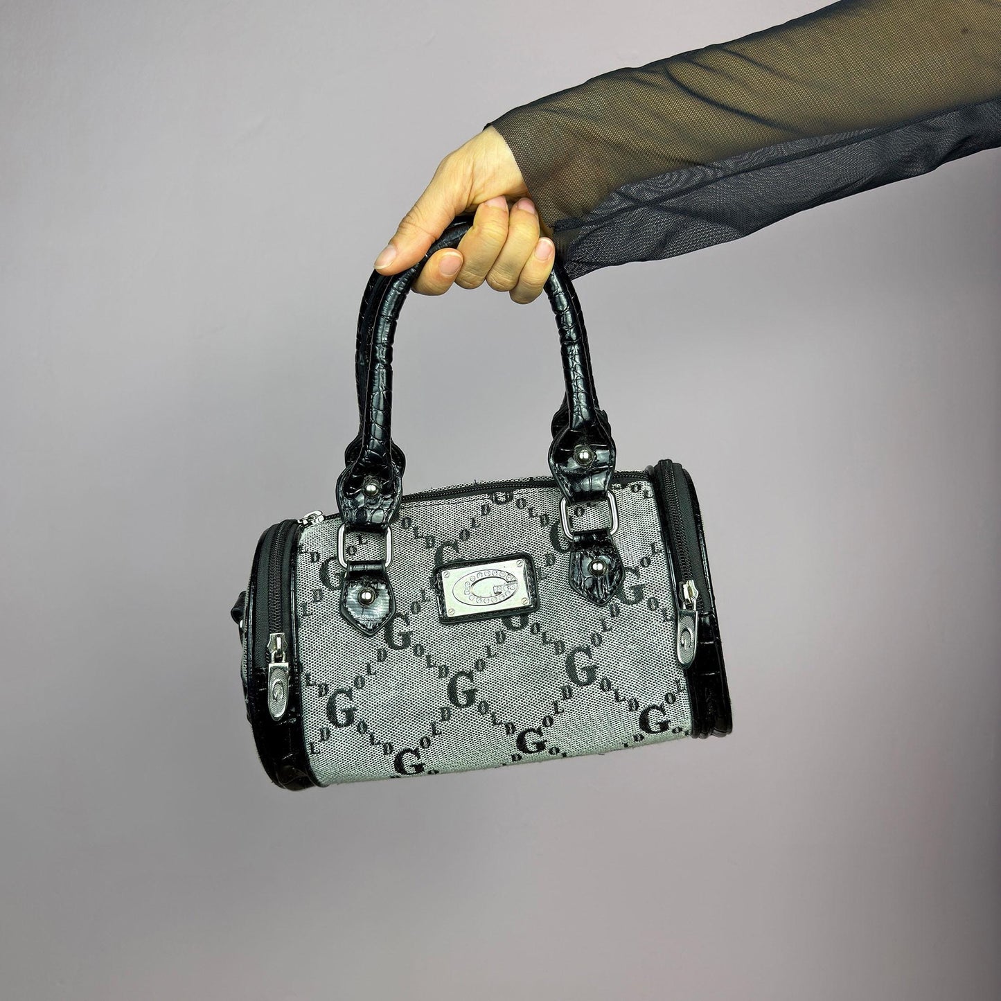 The Y2K Monogram Mini Duffel Bag is a stylish vintage 2000s accessory. Featuring a structured silhouette with an all-over monogram print, sleek black faux patent leather accents, and silver hardware. It includes dual top handles. adult world shop