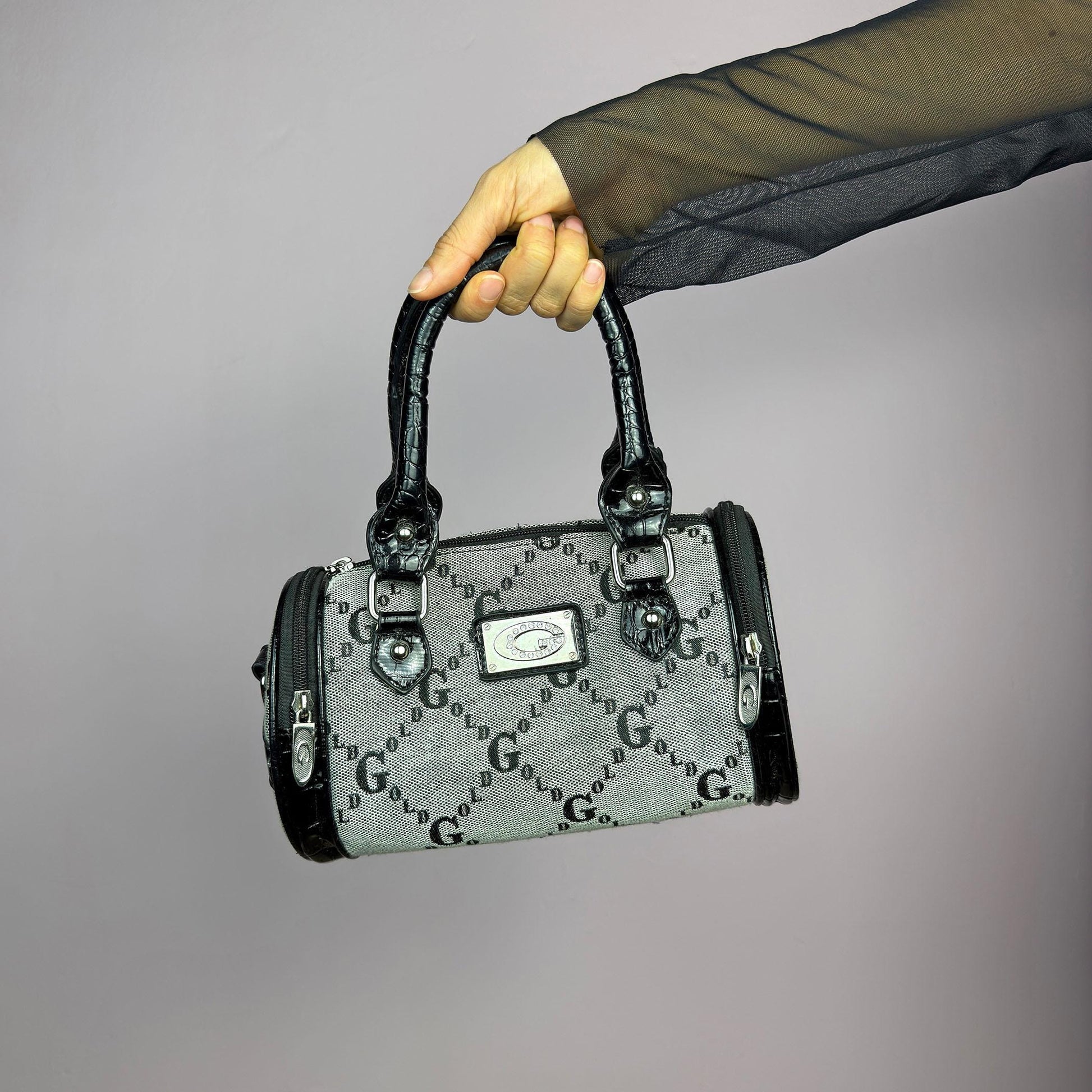 The Y2K Monogram Mini Duffel Bag is a stylish vintage 2000s accessory. Featuring a structured silhouette with an all-over monogram print, sleek black faux patent leather accents, and silver hardware. It includes dual top handles. adult world shop