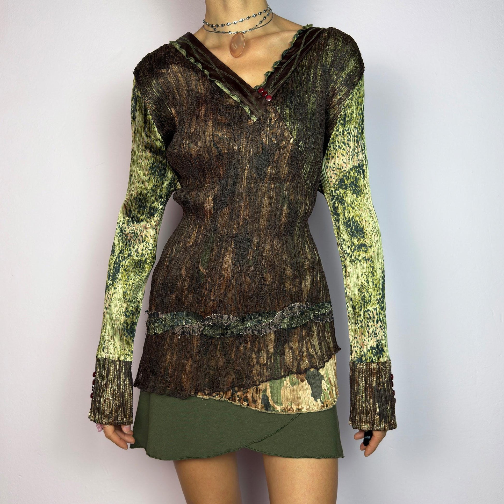 The Y2K Lace Asymmetric Layered Top is a vintage 2000s piece featuring an earthy mix of brown and green tones with a textured, stretchy fabric. This unique top showcases a V-neckline adorned with delicate lace trim, button details. adult world shop