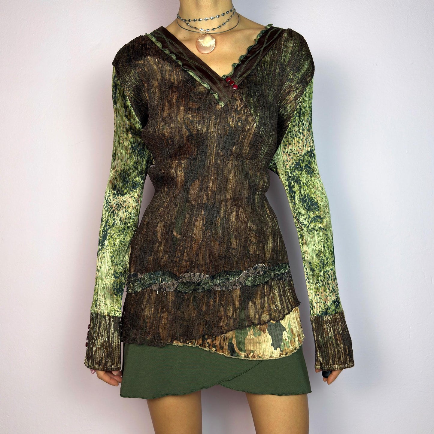 The Y2K Lace Asymmetric Layered Top is a vintage 2000s piece featuring an earthy mix of brown and green tones with a textured, stretchy fabric. This unique top showcases a V-neckline adorned with delicate lace trim, button details. adult world shop