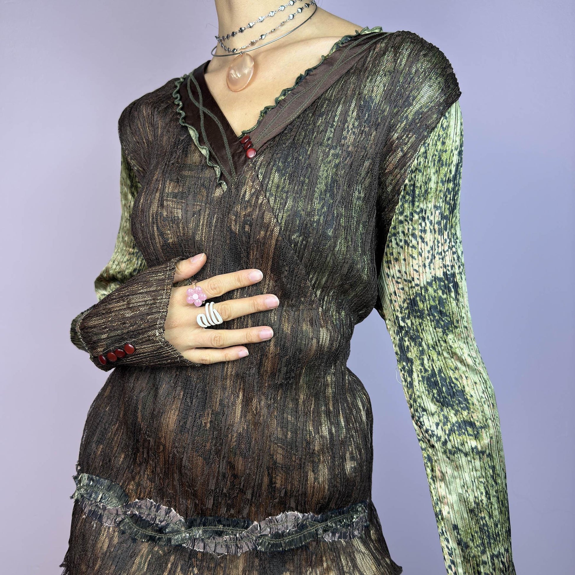 The Y2K Lace Asymmetric Layered Top is a vintage 2000s piece featuring an earthy mix of brown and green tones with a textured, stretchy fabric. This unique top showcases a V-neckline adorned with delicate lace trim, button details. adult world shop