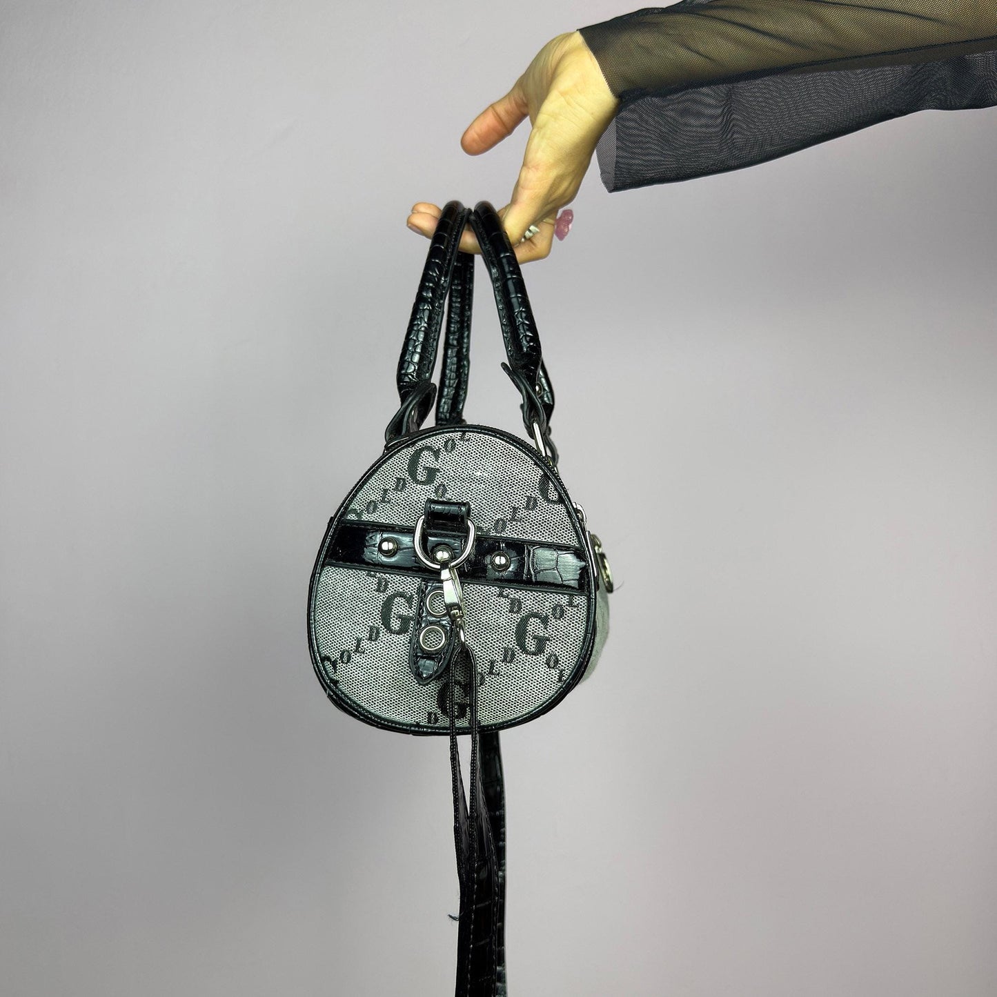 The Y2K Monogram Mini Duffel Bag is a stylish vintage 2000s accessory. Featuring a structured silhouette with an all-over monogram print, sleek black faux patent leather accents, and silver hardware. It includes dual top handles. adult world shop