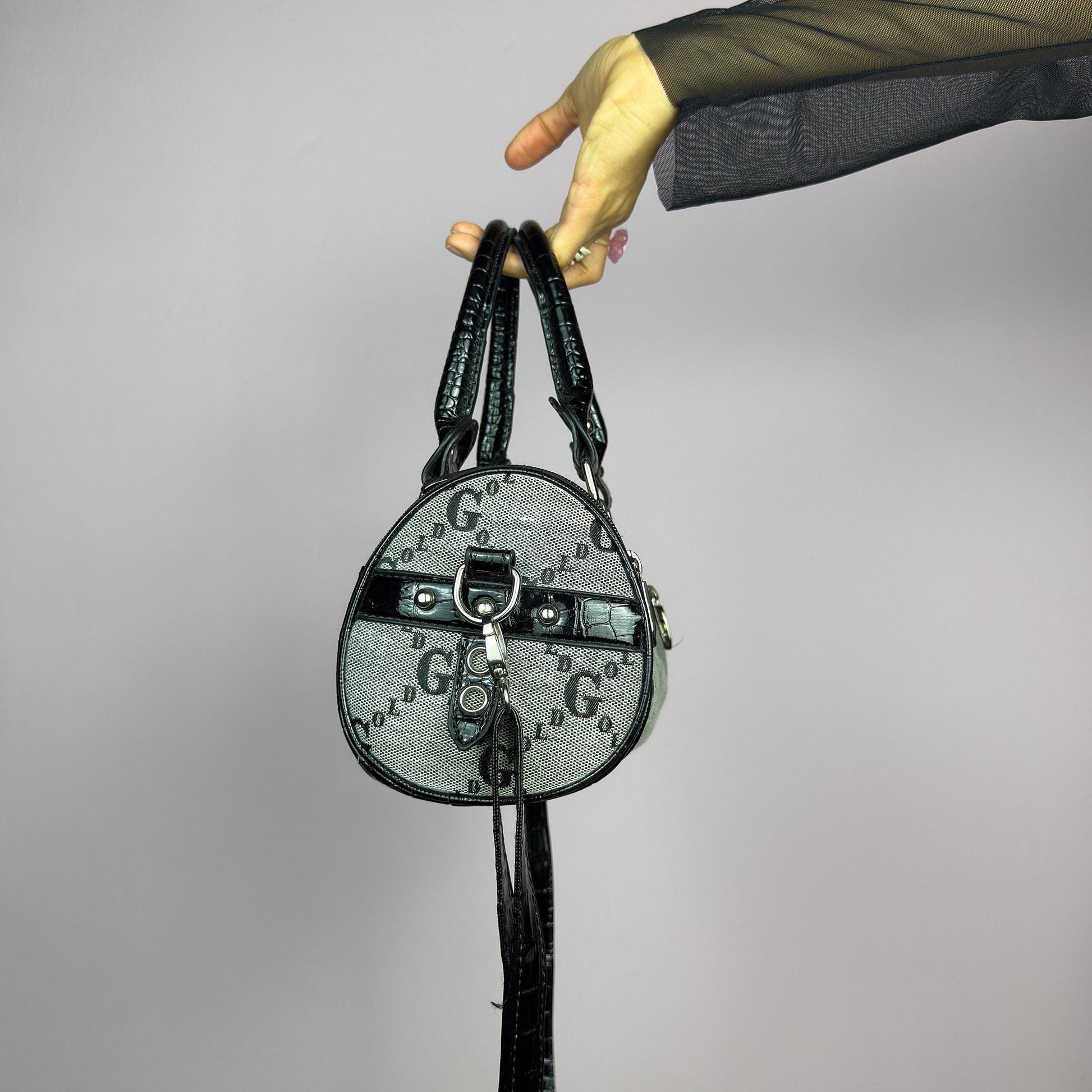 The Y2K Monogram Mini Duffel Bag is a stylish vintage 2000s accessory. Featuring a structured silhouette with an all-over monogram print, sleek black faux patent leather accents, and silver hardware. It includes dual top handles. adult world shop