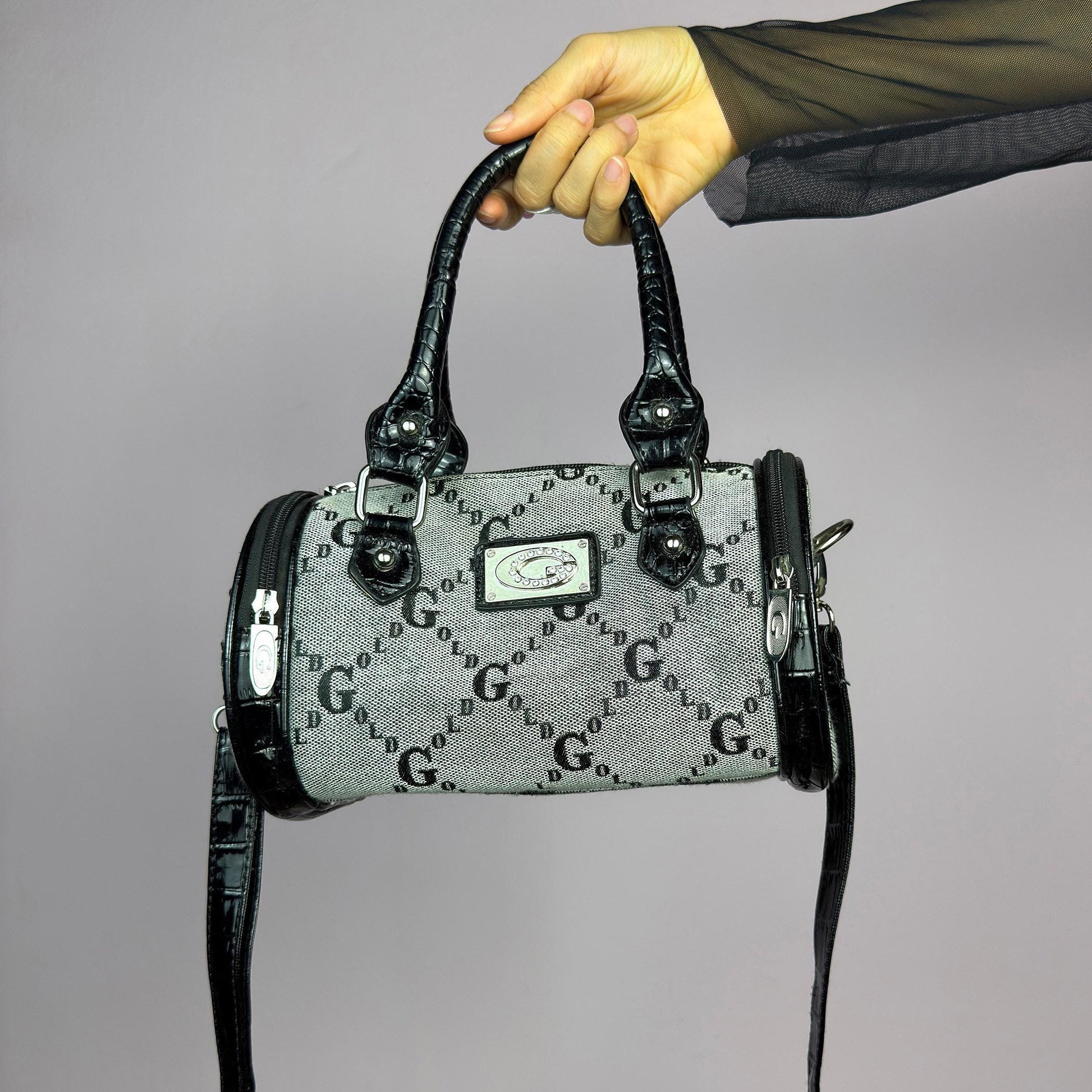 The Y2K Monogram Mini Duffel Bag is a stylish vintage 2000s accessory. Featuring a structured silhouette with an all-over monogram print, sleek black faux patent leather accents, and silver hardware. It includes dual top handles. adult world shop