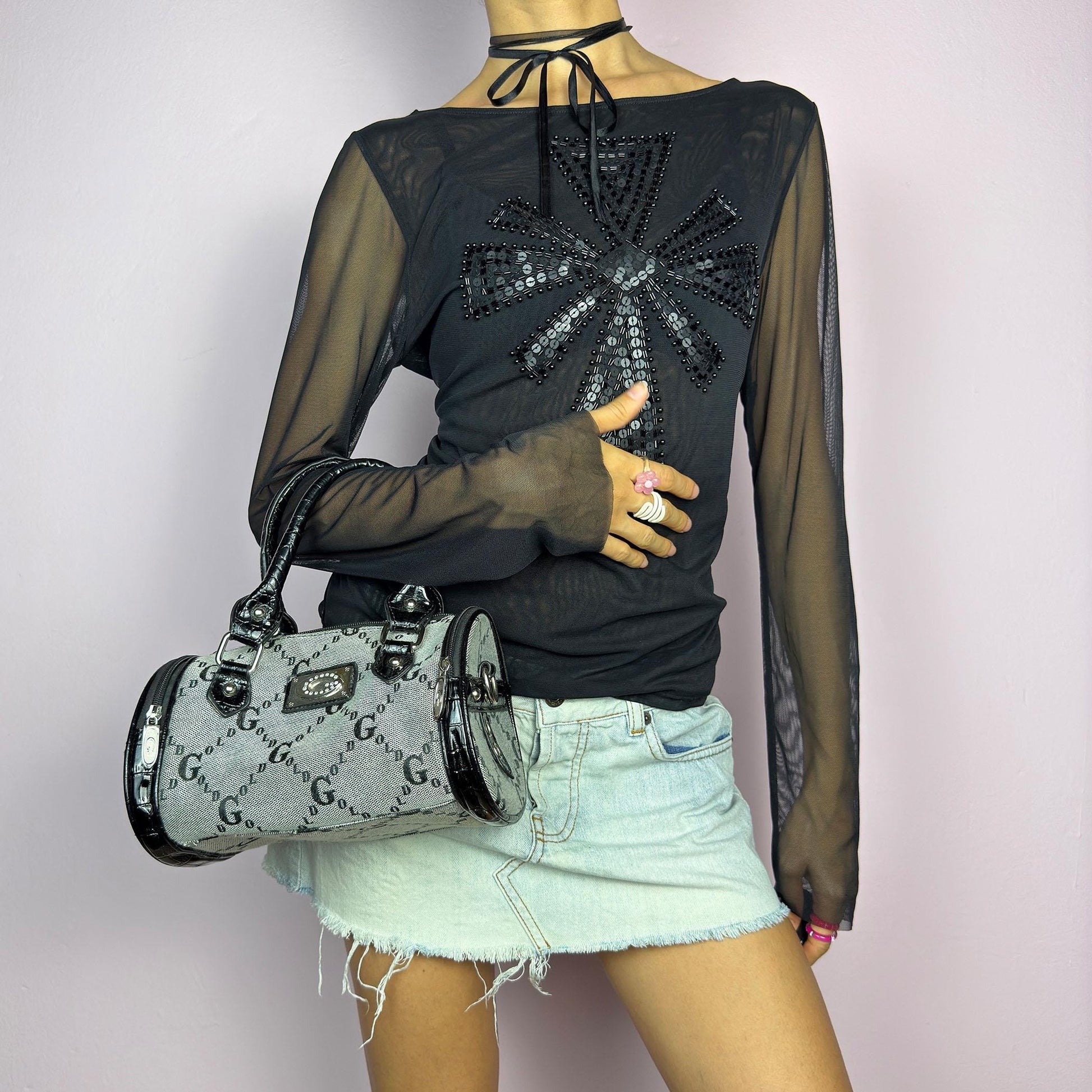 The Y2K Monogram Mini Duffel Bag is a stylish vintage 2000s accessory. Featuring a structured silhouette with an all-over monogram print, sleek black faux patent leather accents, and silver hardware. It includes dual top handles. adult world shop