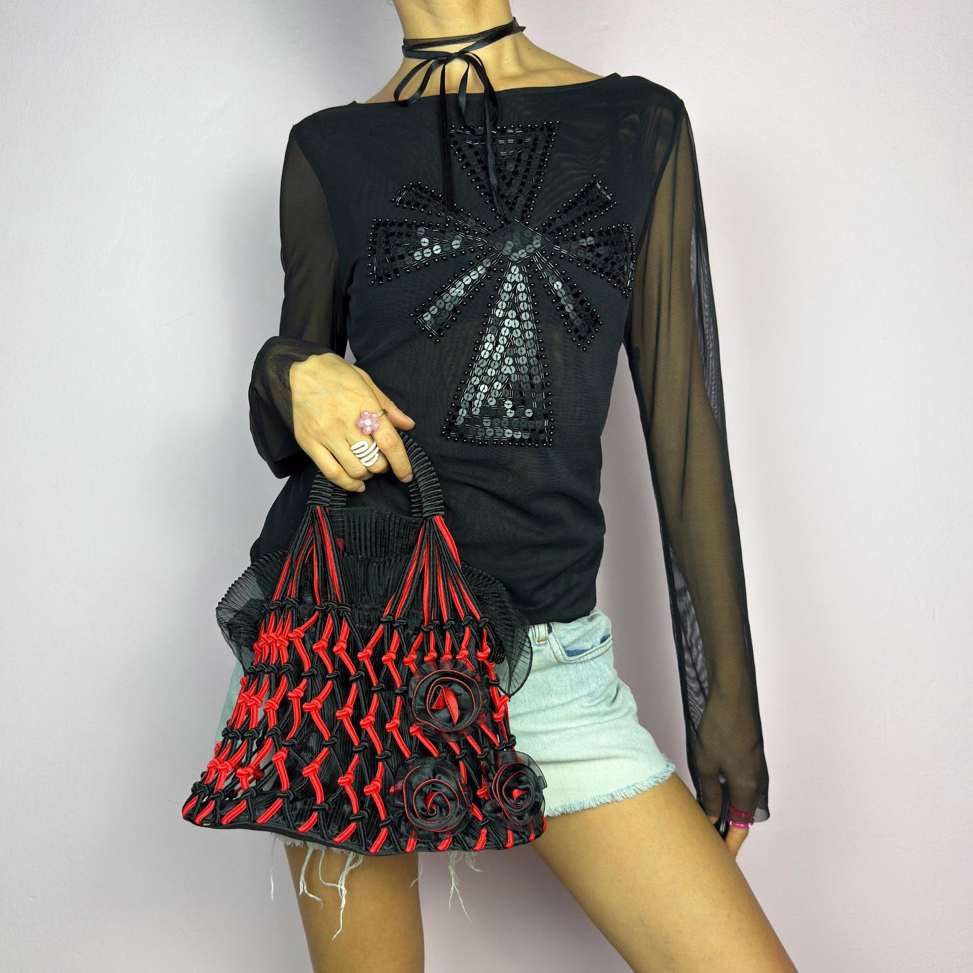 The Vintage 90s Top Handle Drawstring Bag is a unique statement accessory. It features a striking black and red woven design with intricate knot details and decorative rosettes. The semi-structured shape includes a soft. adult world shop
