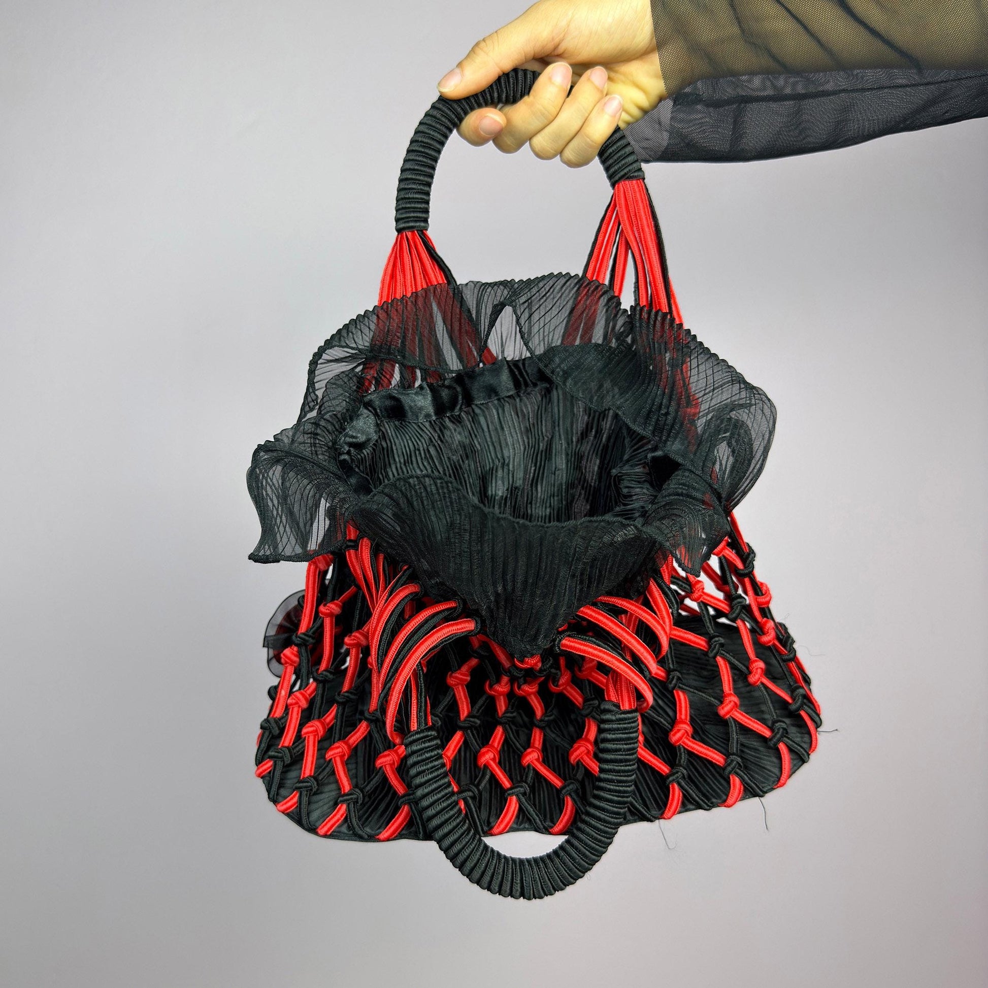 The Vintage 90s Top Handle Drawstring Bag is a unique statement accessory. It features a striking black and red woven design with intricate knot details and decorative rosettes. The semi-structured shape includes a soft. adult world shop