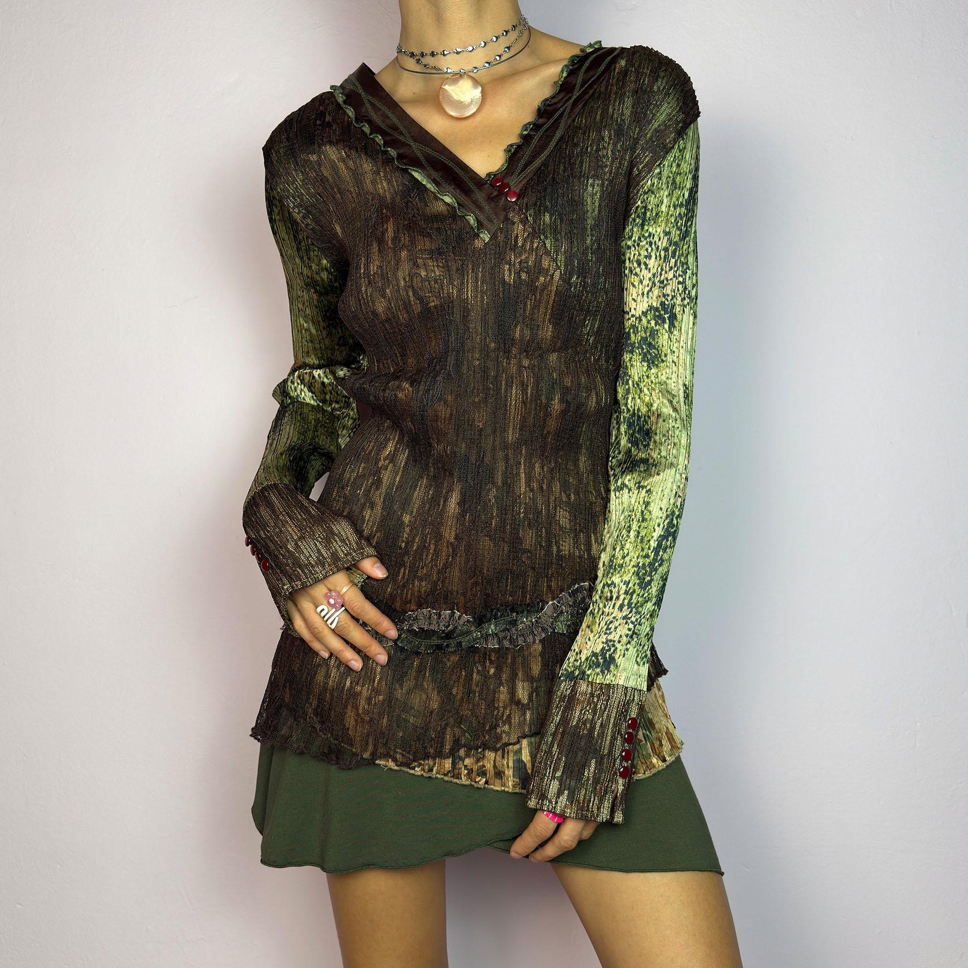 The Y2K Lace Asymmetric Layered Top is a vintage 2000s piece featuring an earthy mix of brown and green tones with a textured, stretchy fabric. This unique top showcases a V-neckline adorned with delicate lace trim, button details. adult world shop