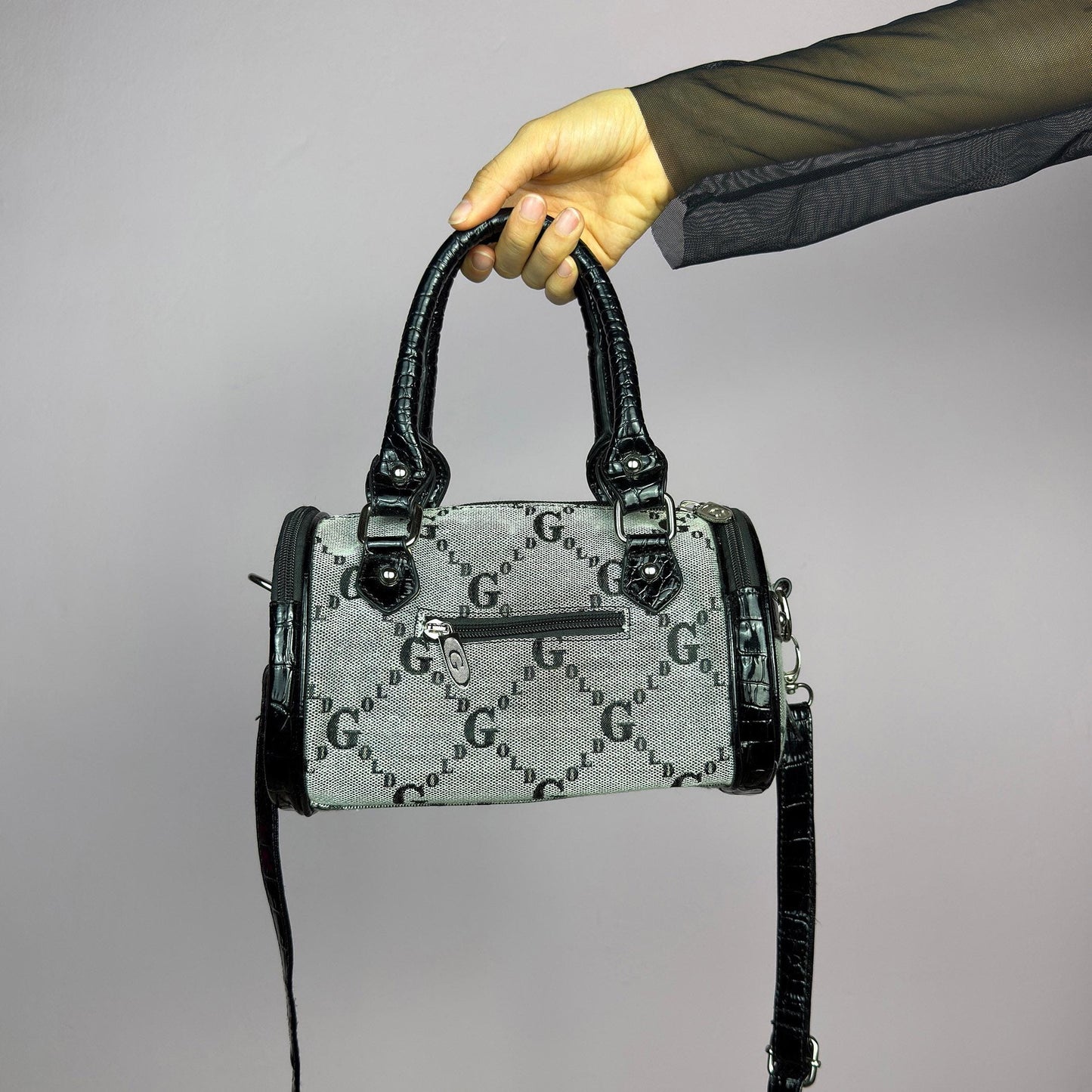 The Y2K Monogram Mini Duffel Bag is a stylish vintage 2000s accessory. Featuring a structured silhouette with an all-over monogram print, sleek black faux patent leather accents, and silver hardware. It includes dual top handles. adult world shop
