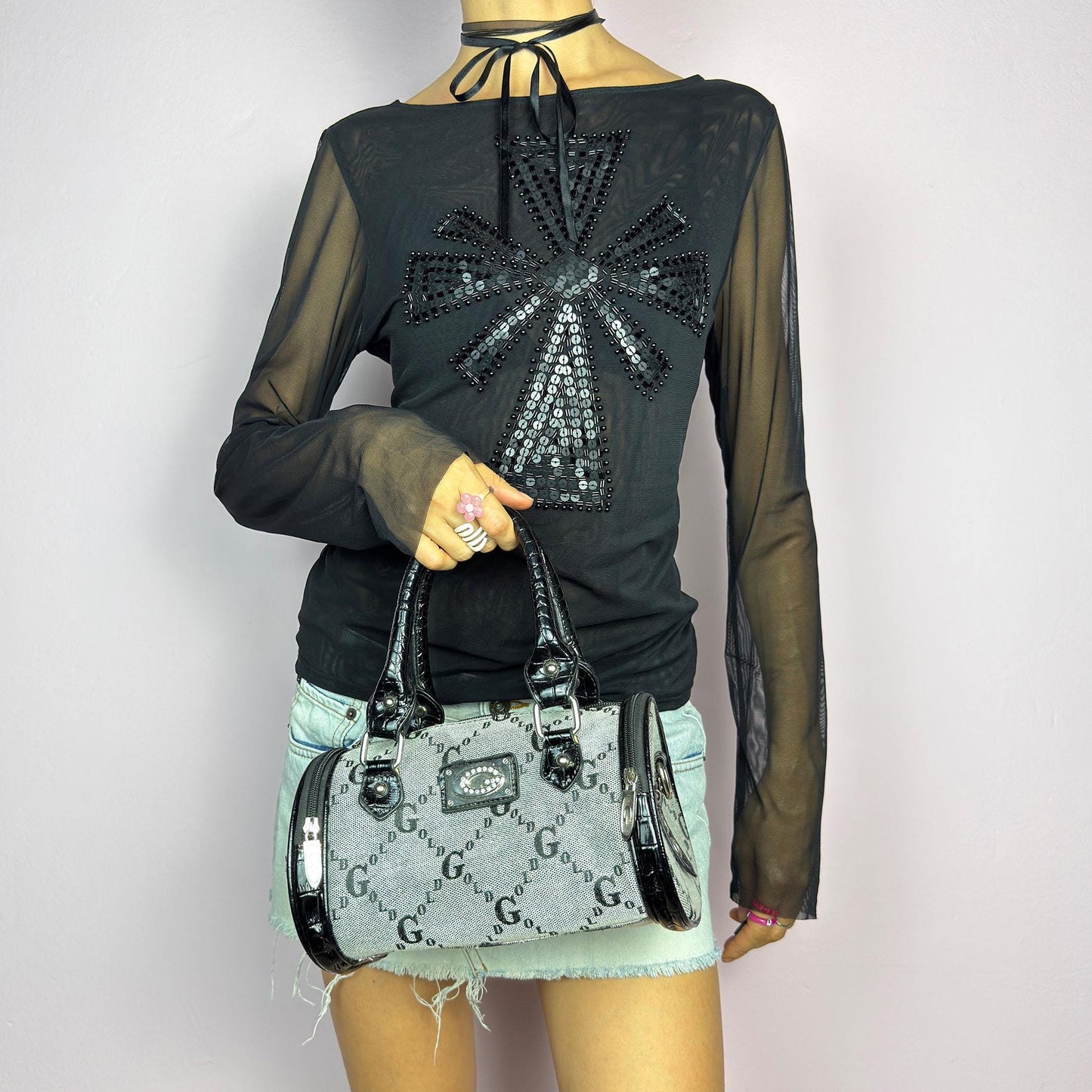 The Y2K Monogram Mini Duffel Bag is a stylish vintage 2000s accessory. Featuring a structured silhouette with an all-over monogram print, sleek black faux patent leather accents, and silver hardware. It includes dual top handles. adult world shop