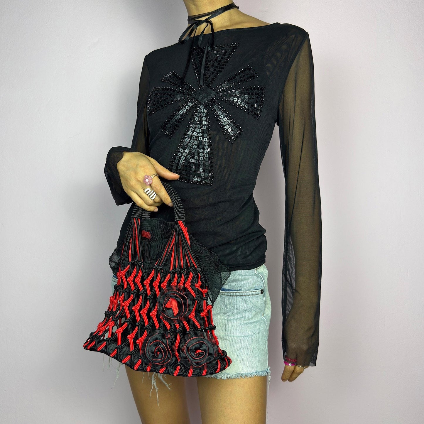 The Vintage 90s Top Handle Drawstring Bag is a unique statement accessory. It features a striking black and red woven design with intricate knot details and decorative rosettes. The semi-structured shape includes a soft. adult world shop