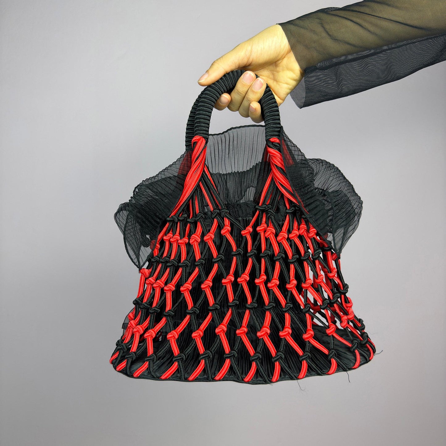 The Vintage 90s Top Handle Drawstring Bag is a unique statement accessory. It features a striking black and red woven design with intricate knot details and decorative rosettes. The semi-structured shape includes a soft. adult world shop