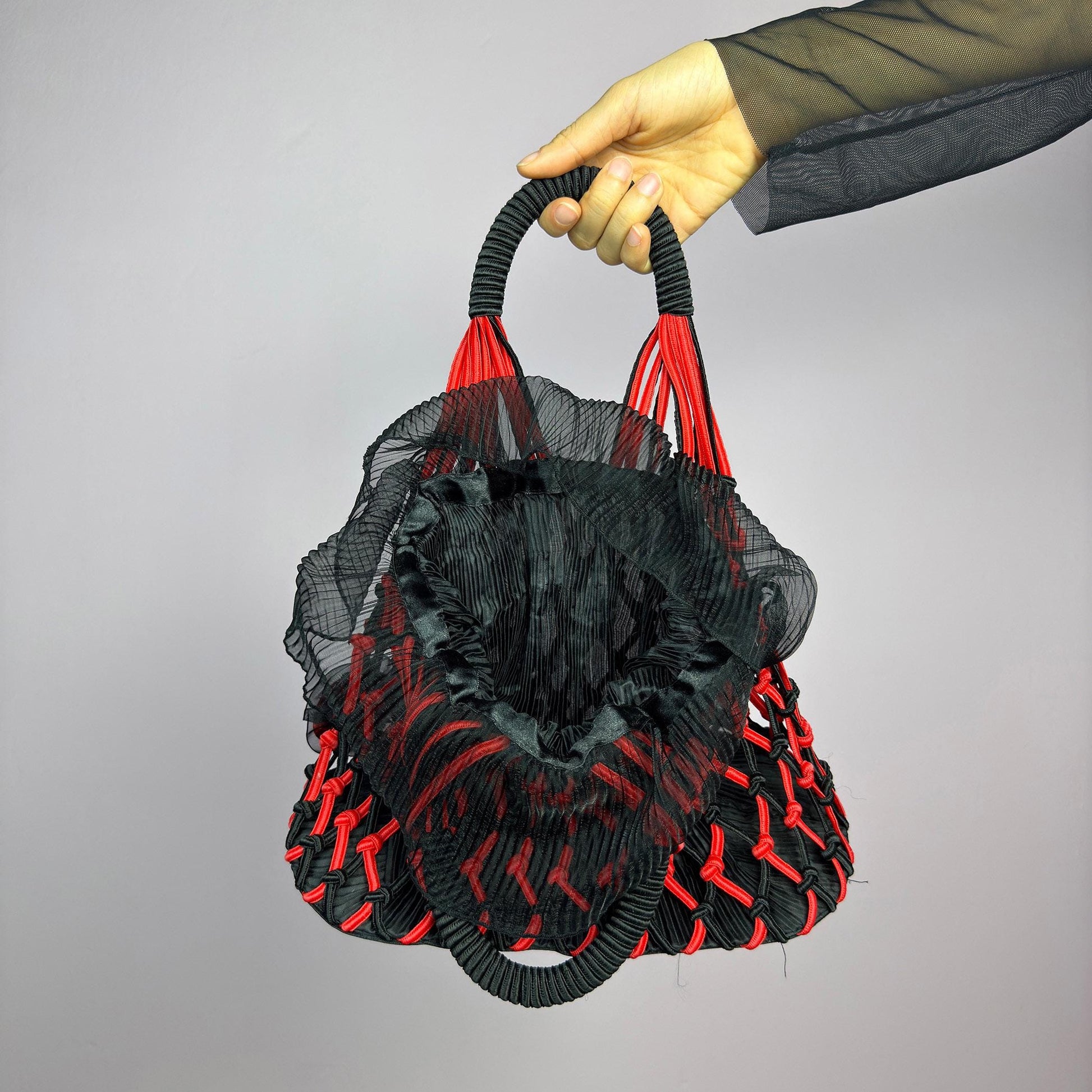 The Vintage 90s Top Handle Drawstring Bag is a unique statement accessory. It features a striking black and red woven design with intricate knot details and decorative rosettes. The semi-structured shape includes a soft. adult world shop